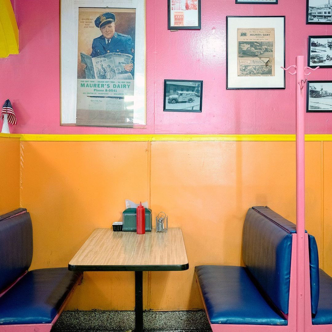 small blue booths and a wood laminate table. brightly saturated pink, yellow, and orange walls with a photographs on the wall