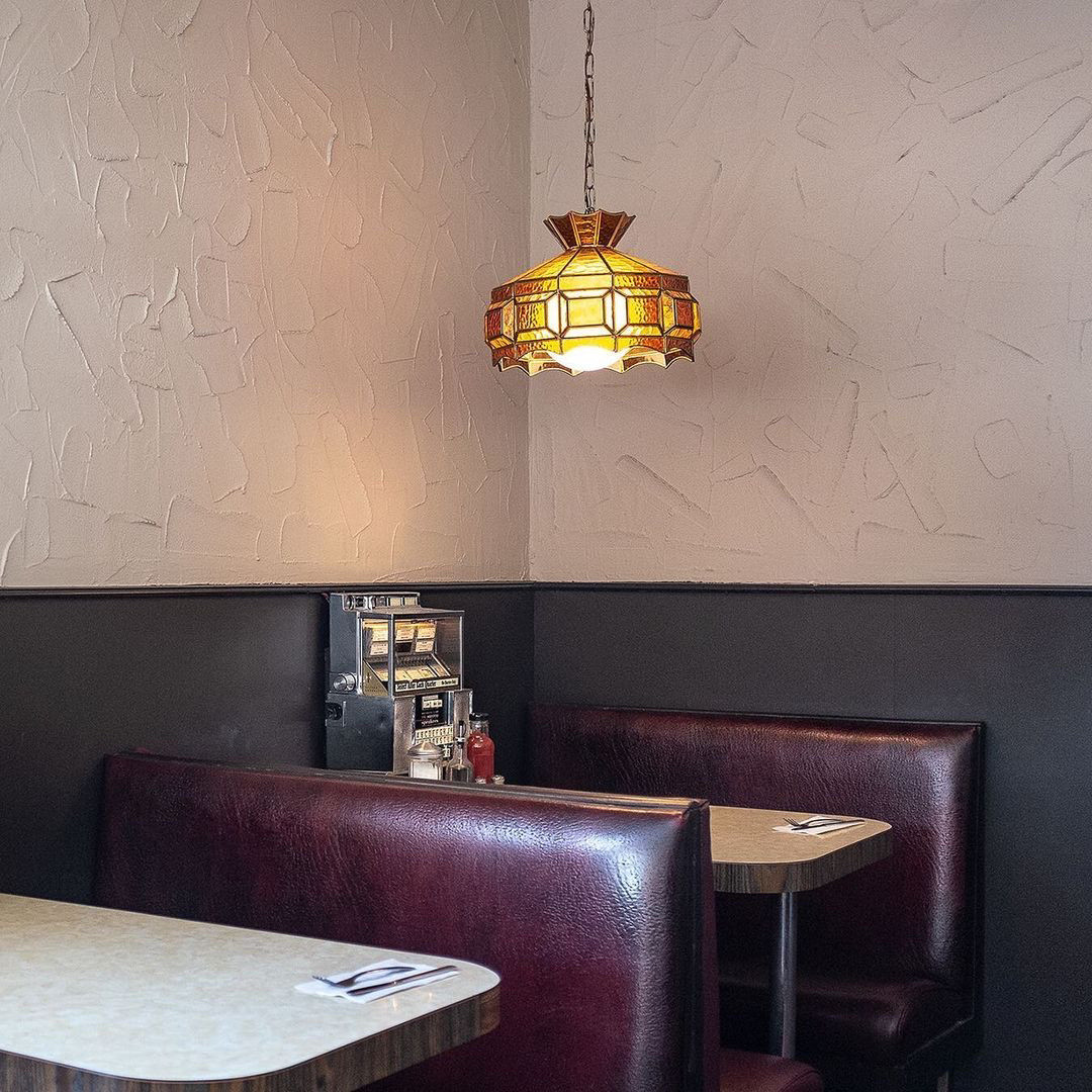 maroon/burgundy leather booth seats and a vinyl laminate table, small stained glass chandelier, and a small jukebox on the table