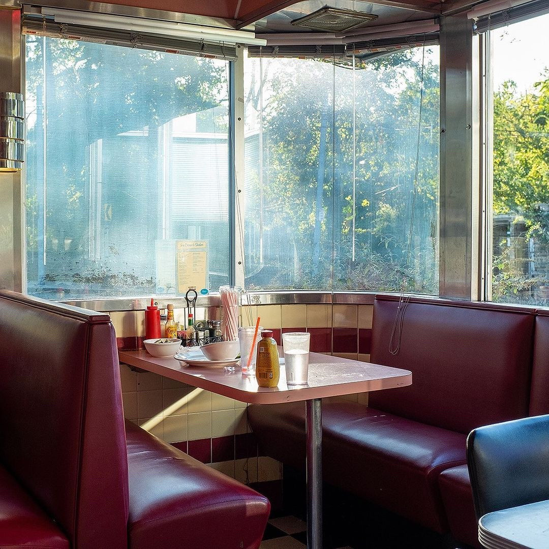 a corner table with large windows with metal framing. dark red vinyl booths and light pink tables.