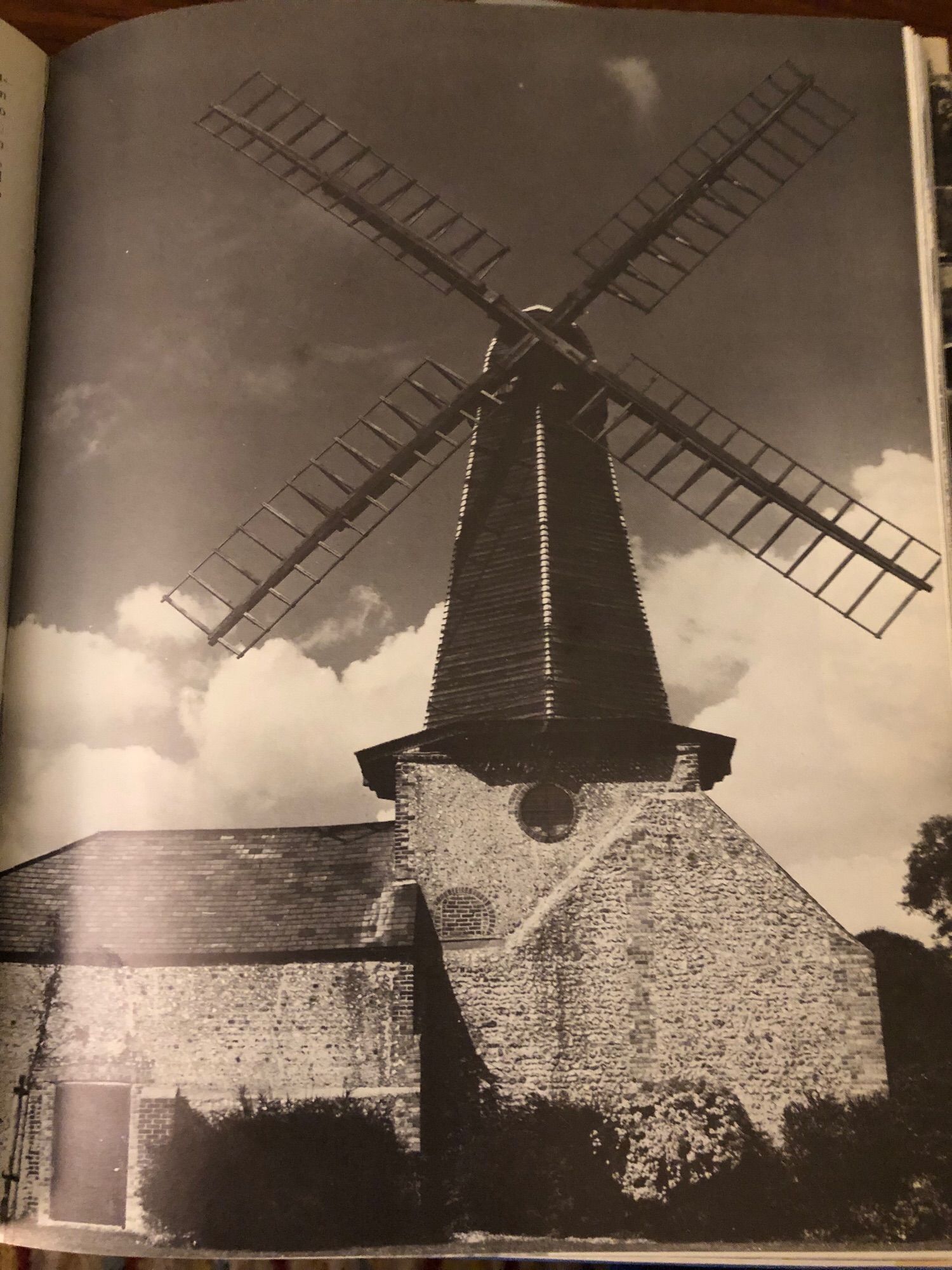 Photo of a black and white photo in a book of the windmill at Blatchington West in East Sussex. Looks like someone whacked a set of windmill blades on the spire of a flint church