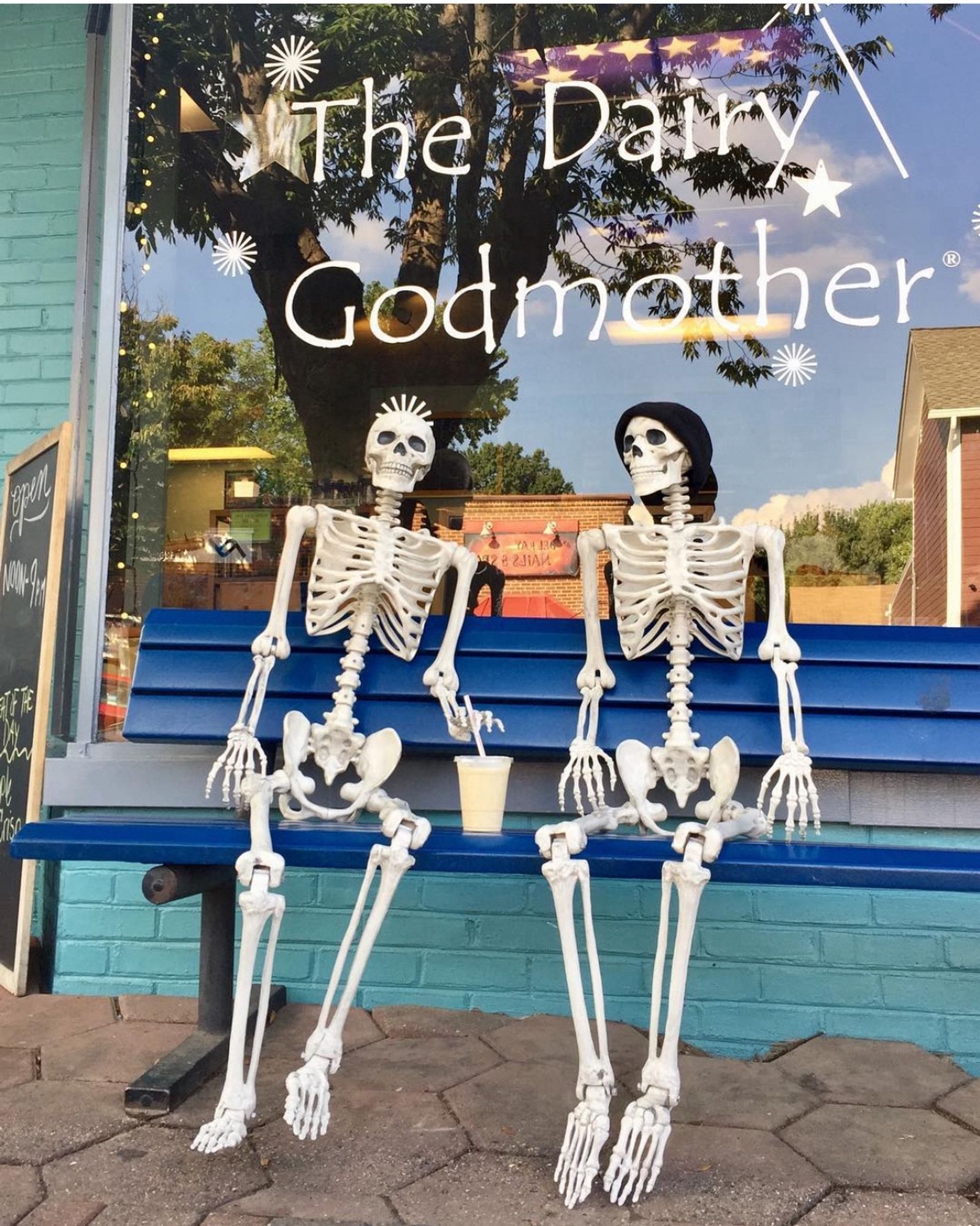 A pair of plastic Halloween skeletons sit on a blue bench in front of The Dairy Godmother with a milkshake. (Please note: This photo is from 2016 and this Alexandria, Virginia storefront has changed slightly).