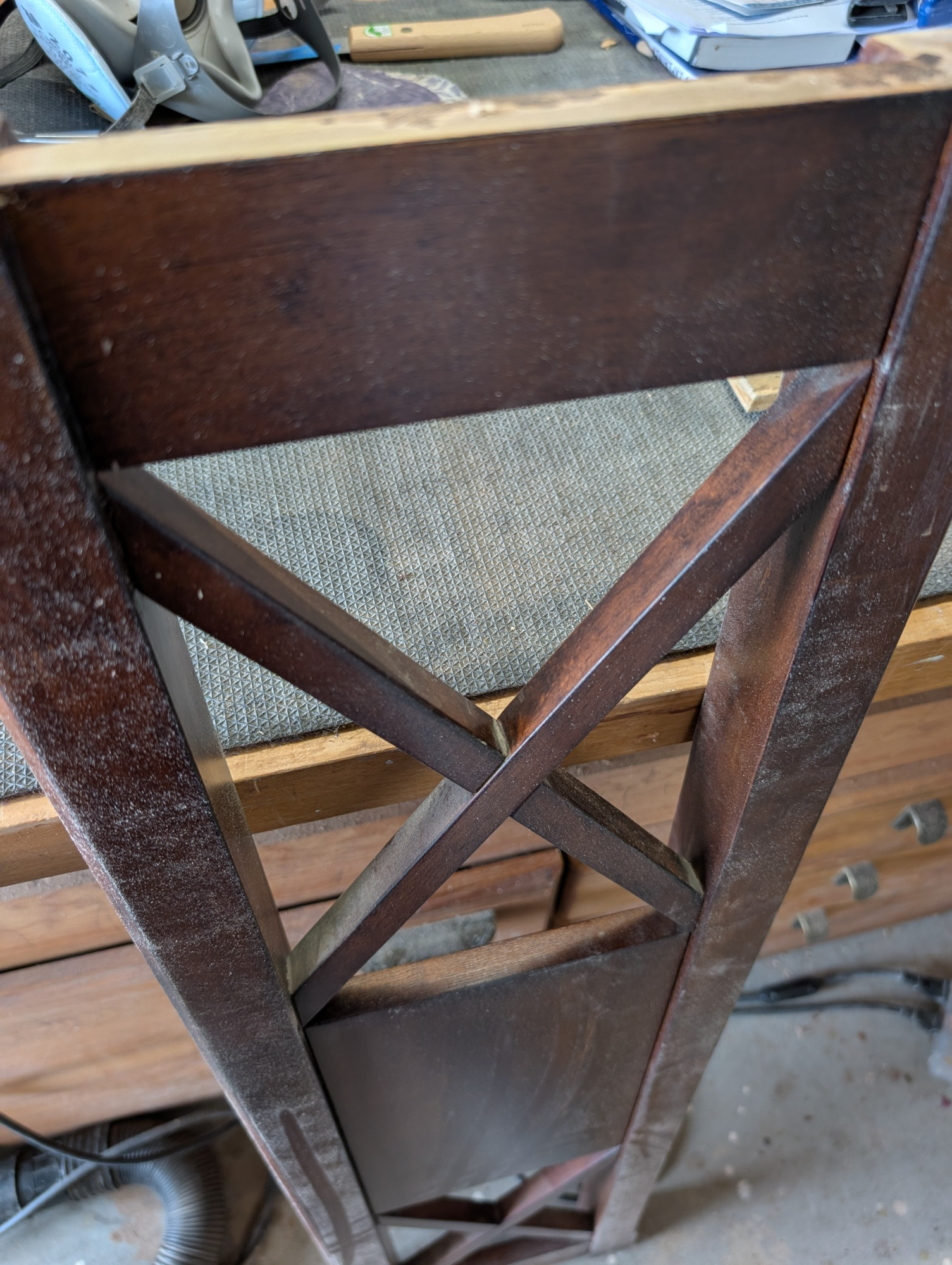 A piece of a wooden shelf arranged with an X shaped brace. It's finished with a dark brown dye and varnish