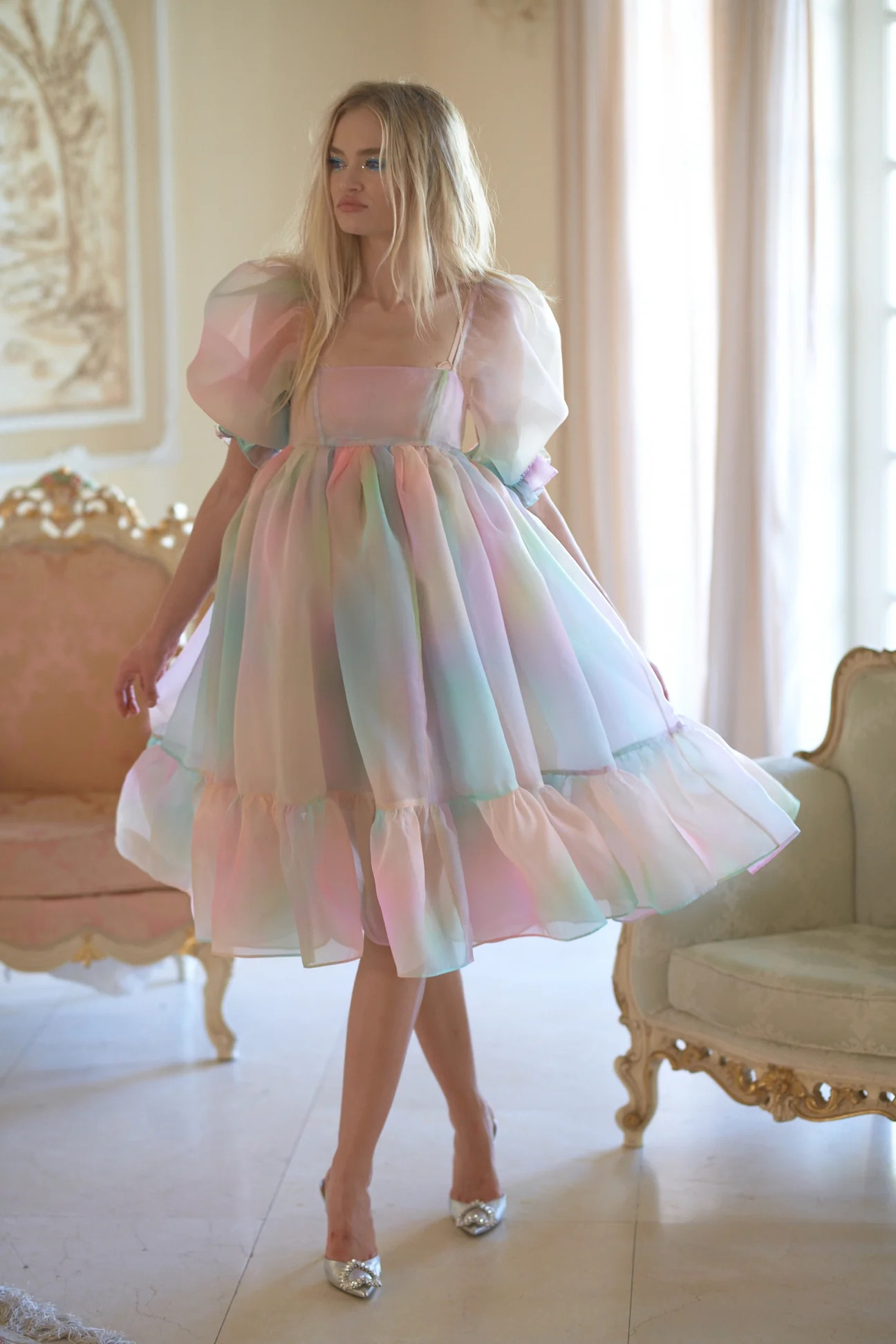 pastel rainbow puff dress with a fitted top and puff sleeves. there are two fancy chairs in the background, one white with gold trim and one pink with either white or gold trim and there is a painting hung on the cream wall and large windows with light blush curtains hanging down from the floor in a white marble tiled floor room, very elegant. 

Item description from website:
This gorgeously frothy dress is perfect for spinning through the city, dancing on roof tops, or standing out at the party. Imagined in Italy, dancing barefoot on the Trevi fountain...

A spin on the classic, now a full length midi puff dress! It's big, actually it's yards and yards and yaaards of fabric. This major puff has a full circle skirt so you can do full numbers of spins singing "the hills are alive with the sound of music" 

Sheer bandeau puff dress
Center back zipper closure 
Three layers of pleated organza skirt
Unlined