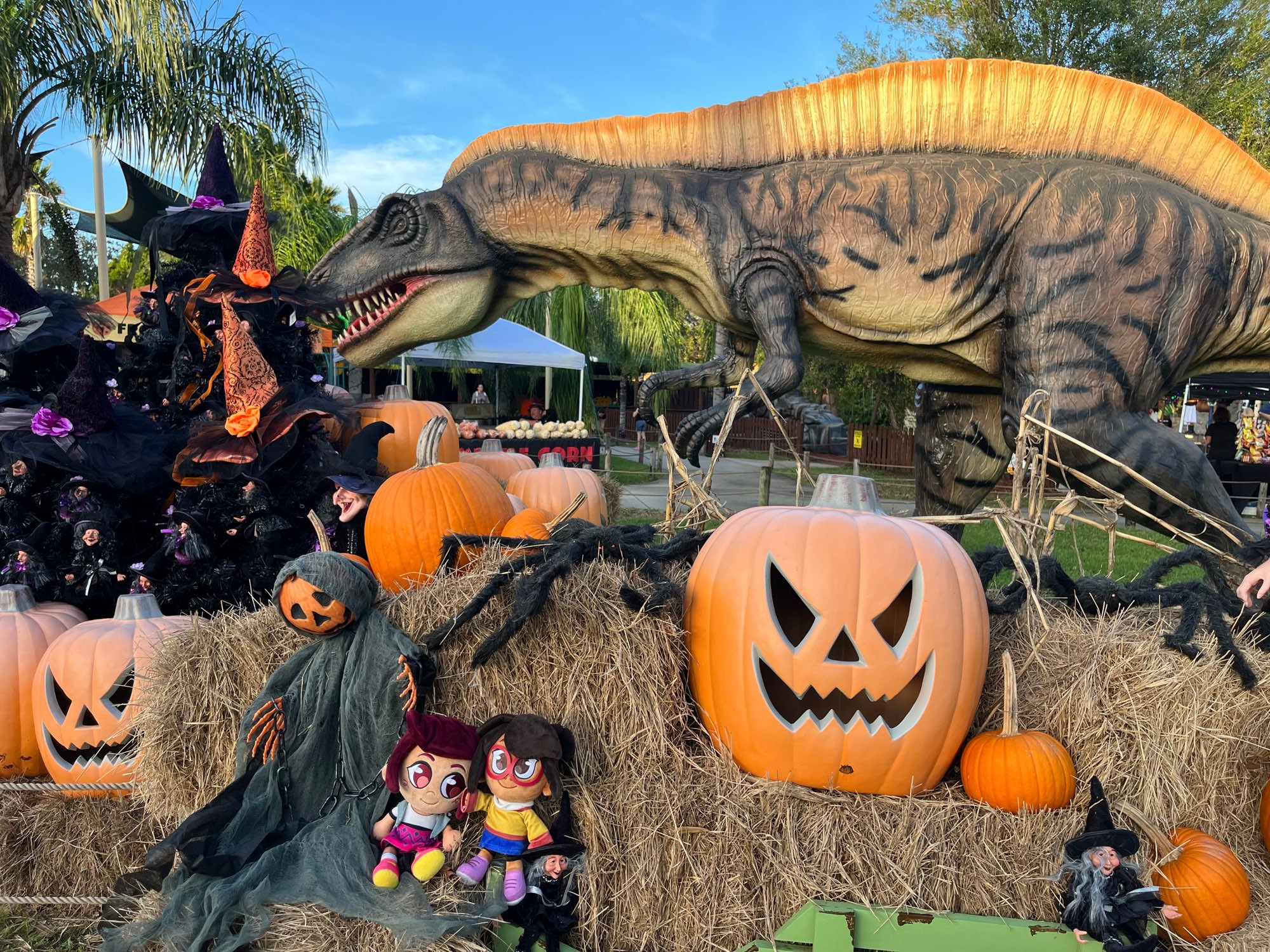 Molly McGee and June Chen plushies in front of Dinosaur dioramas litters with Jack-O-Lanterns and other Halloween decor