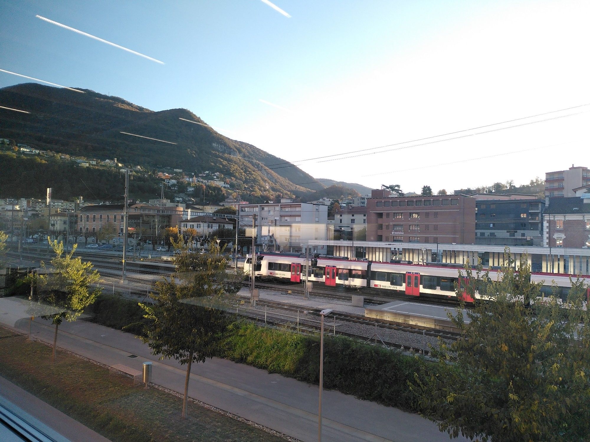 View from the Mendrisio SUPSI building overlooking the train station with hills in the background. The sun is out