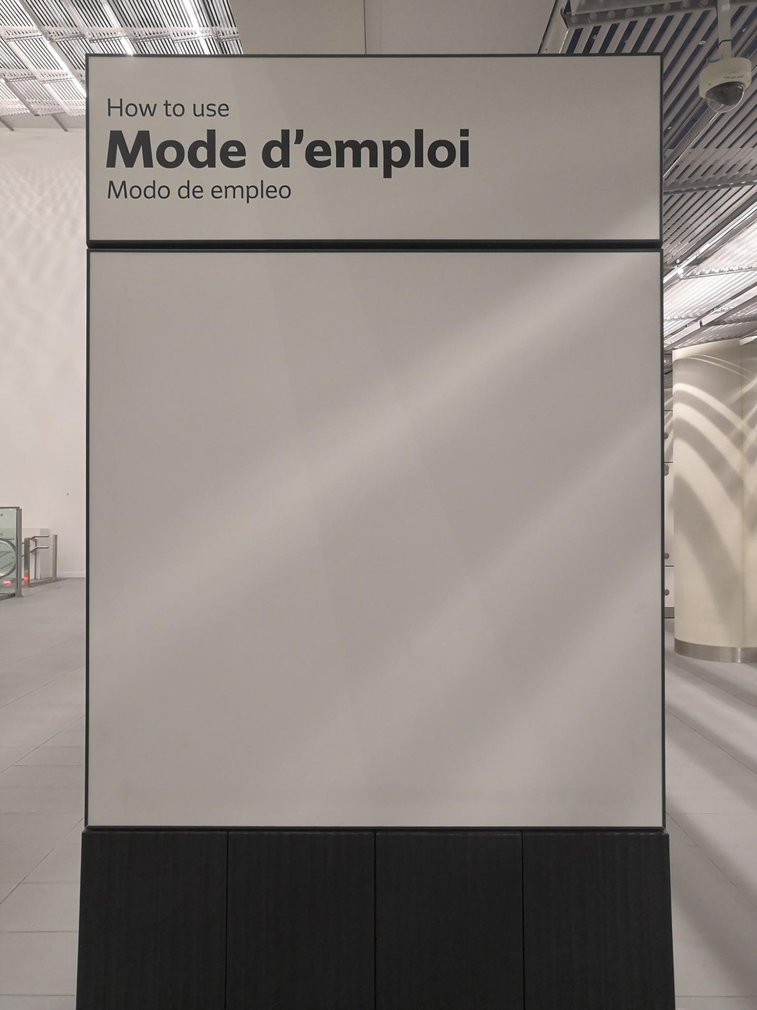 Un panneau type panneau publicitaire sur lequel est inscrit "Mode d'emploi" mais qui est complètement vierge/blanc