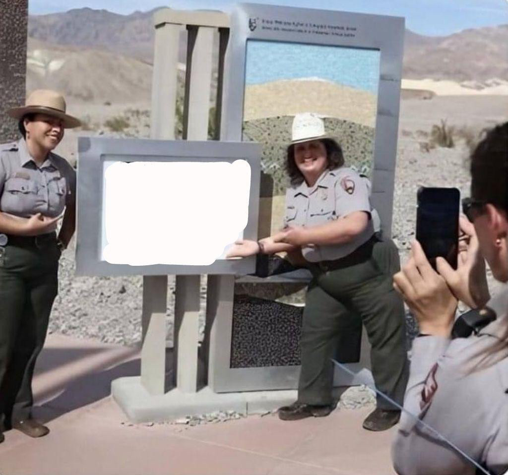 Dans un désert, 2 membres des forces de l'ordre états-uniennes posent et exposent fièrement un panneau (dont le contenu est effacé pour ce meme) pendant qu'un·e troisième les prend en photo