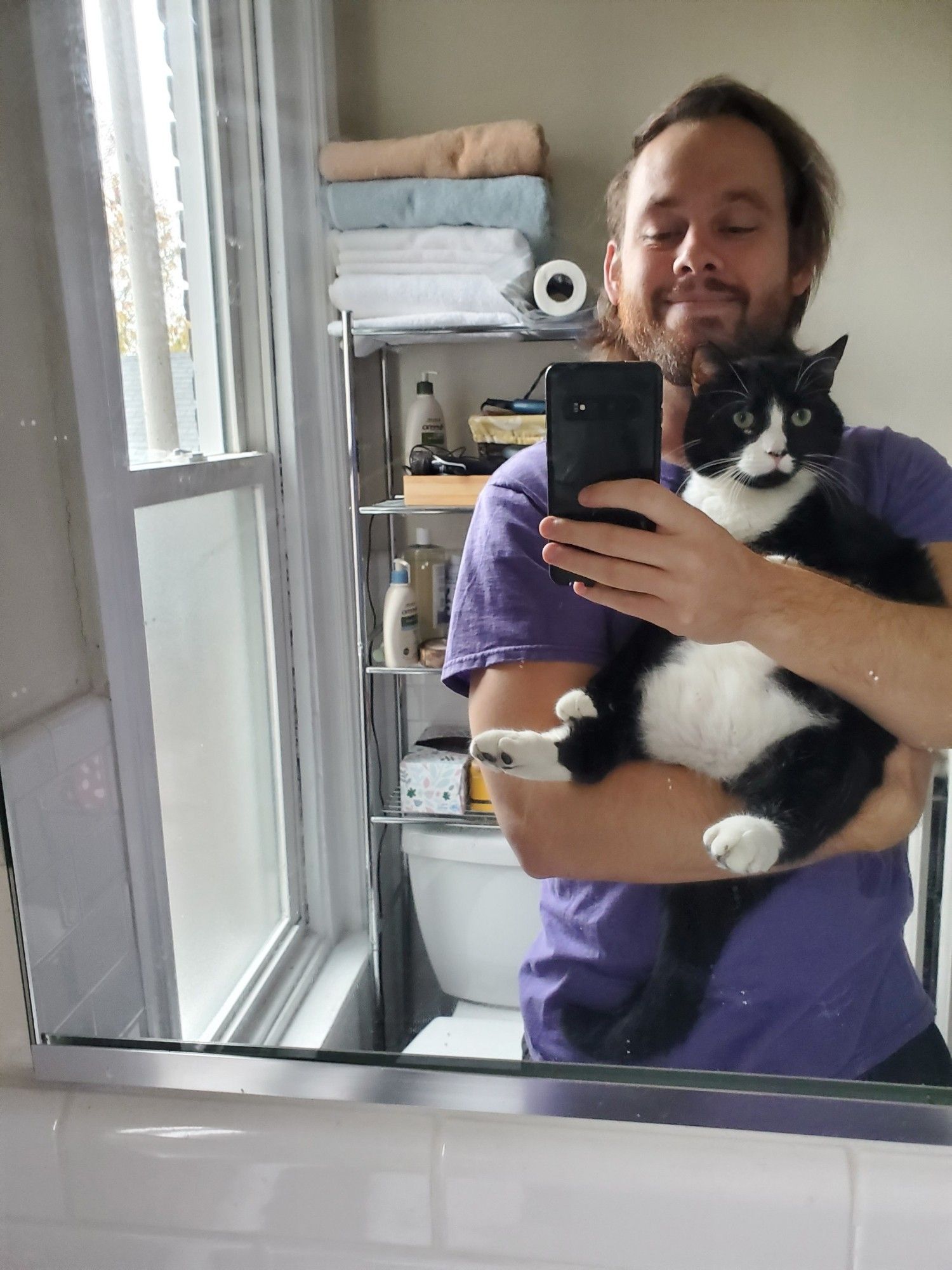 Me in a purple tshirt holding and taking a picture of Fishy, a big tuxedo cat.