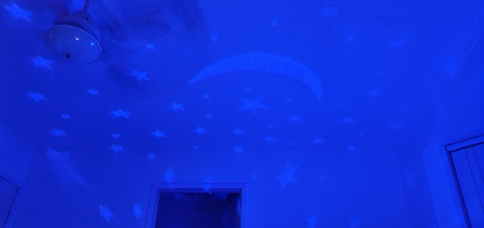 A bedroom with blue lights and lighter blue stars on the ceiling.