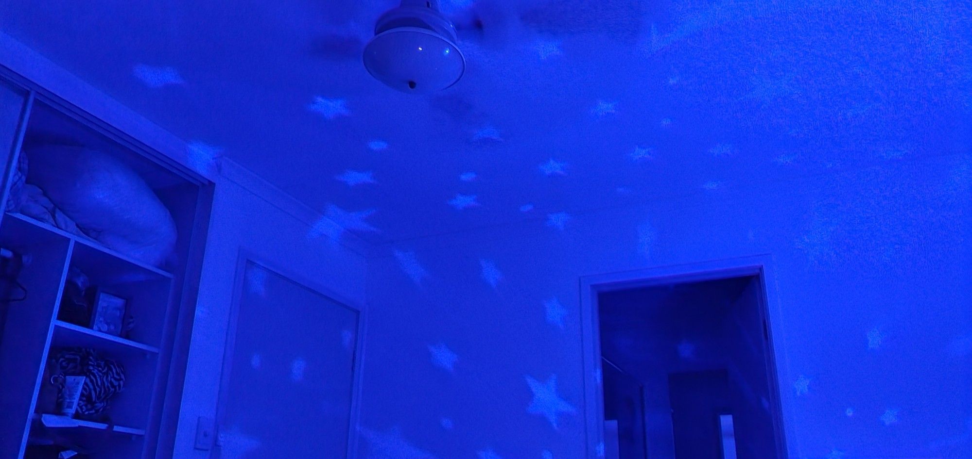 A bedroom with blue lights and lighter blue stars on the ceiling.