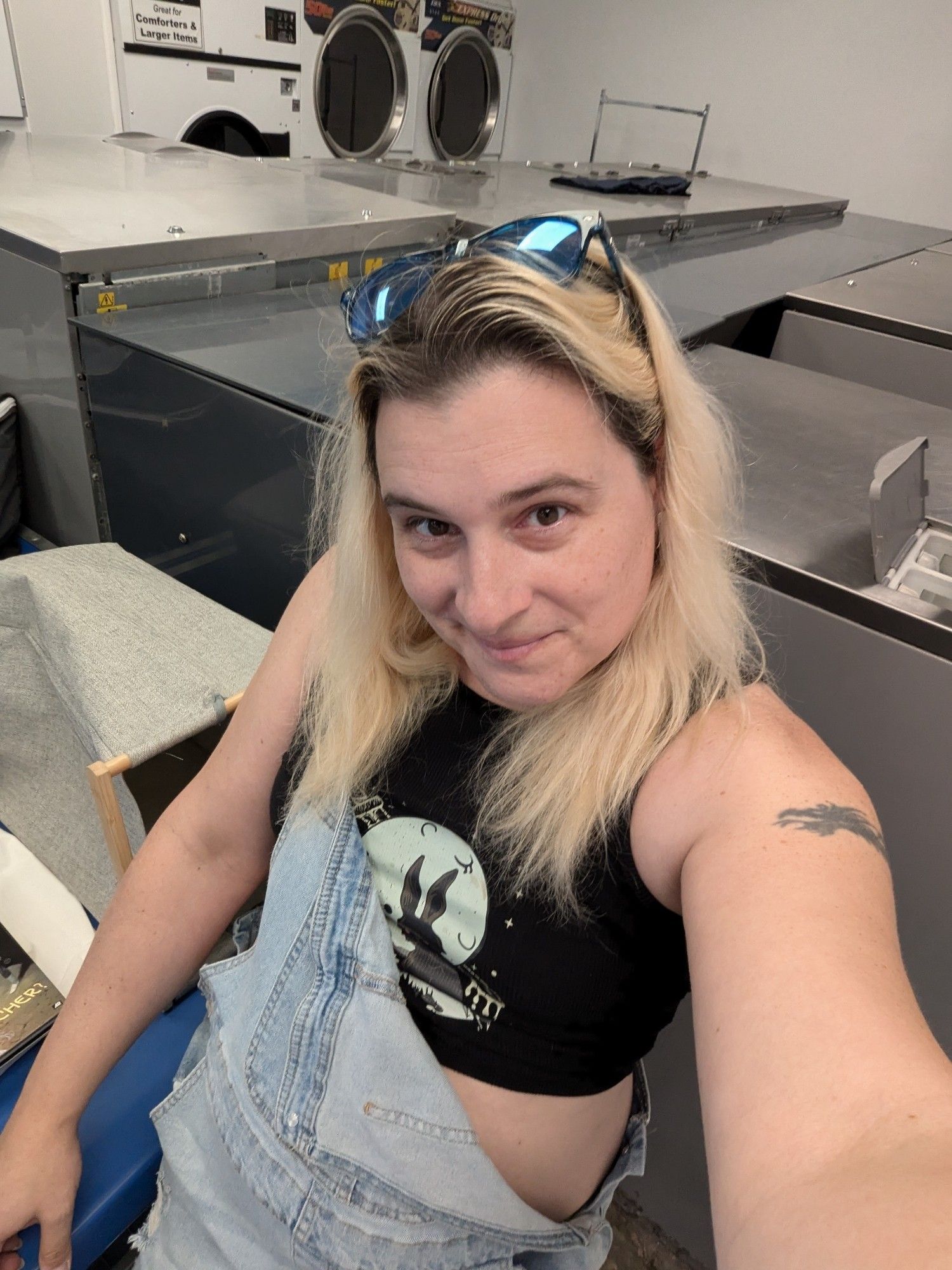 Me in a black crop top, and am overall romper. Visibly at a laundry mat.