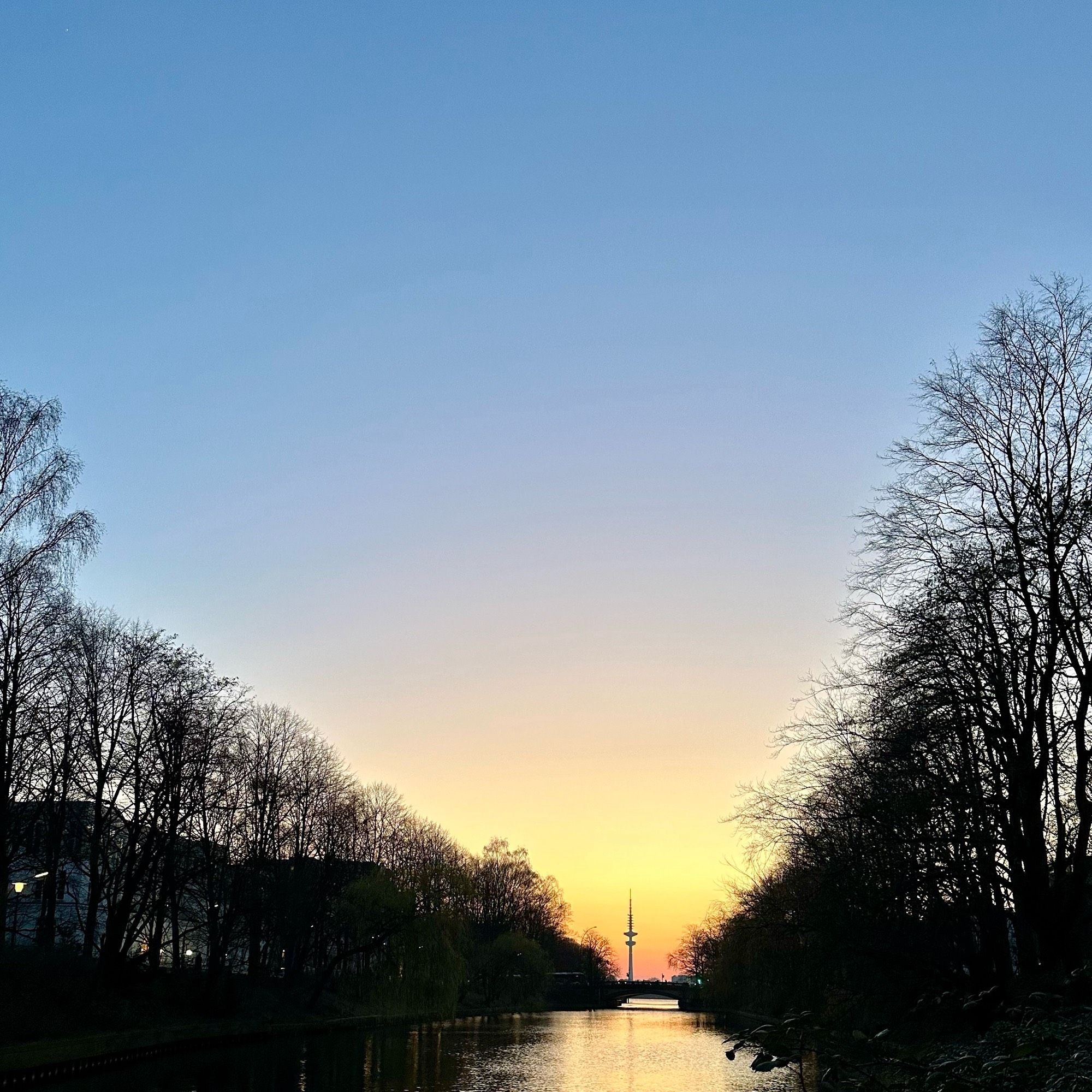 Das Bild zeigt den kleinen Bachlauf Wandse in Hamburg an Ihrer Mündung zur Alster. Im Hintergrund ist der hambuger Fernsehturm vor dem Sonnenuntergang zusehen.