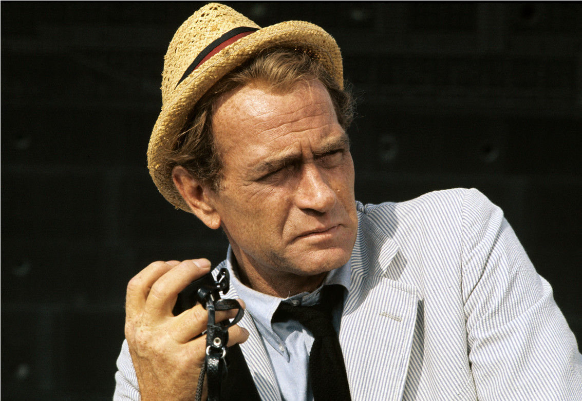 Screenshot of still of actor Darren McGavin from 1974. McGavin is dressed in a white pinstripe suit and wearing one of those straw hats. 