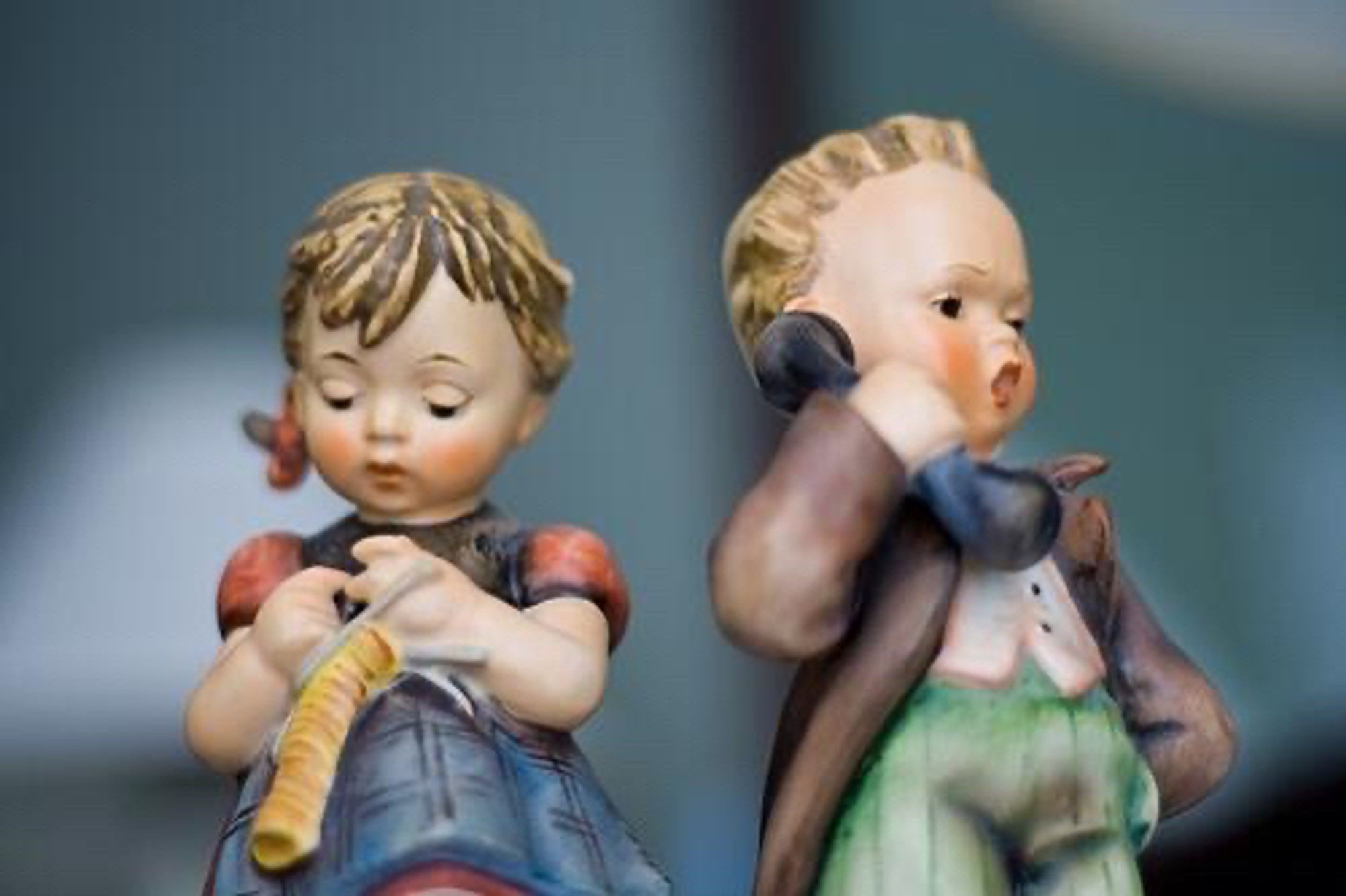 Hummel figurine boy talking on the phone. He looks angry. He is standing next to a Hummel girl who is focused on her knitting.