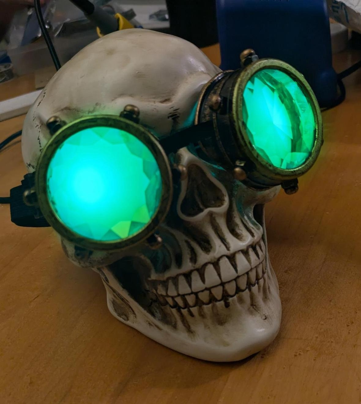 A plastic skull wearing kaleidoscope goggles with green LEDs dressed up to look like Manfred from Dragon age the veilguard