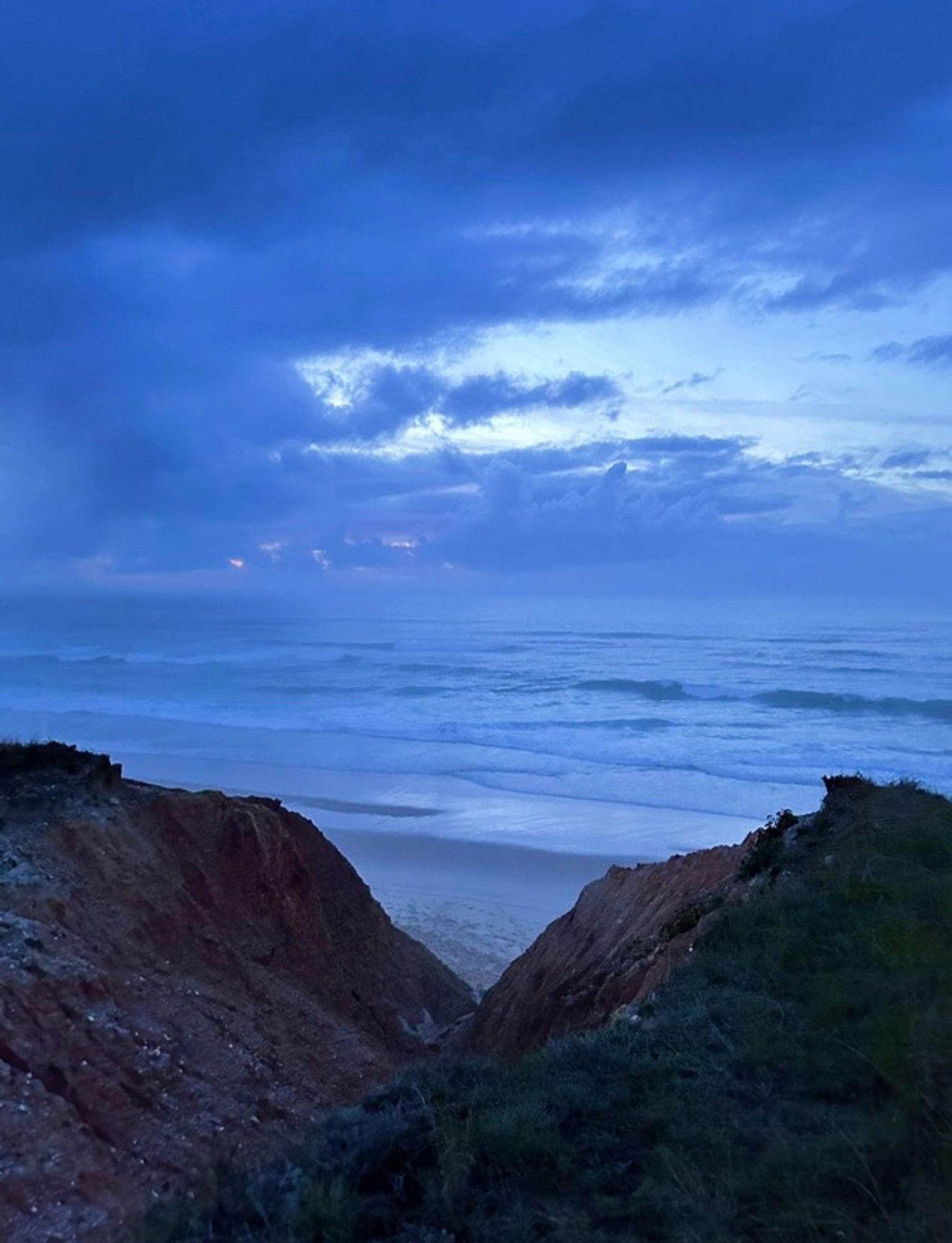 Clouds gather in a tapestry of blue silver-fade with greys of every shade and depth while below large waves signal storms ahead.