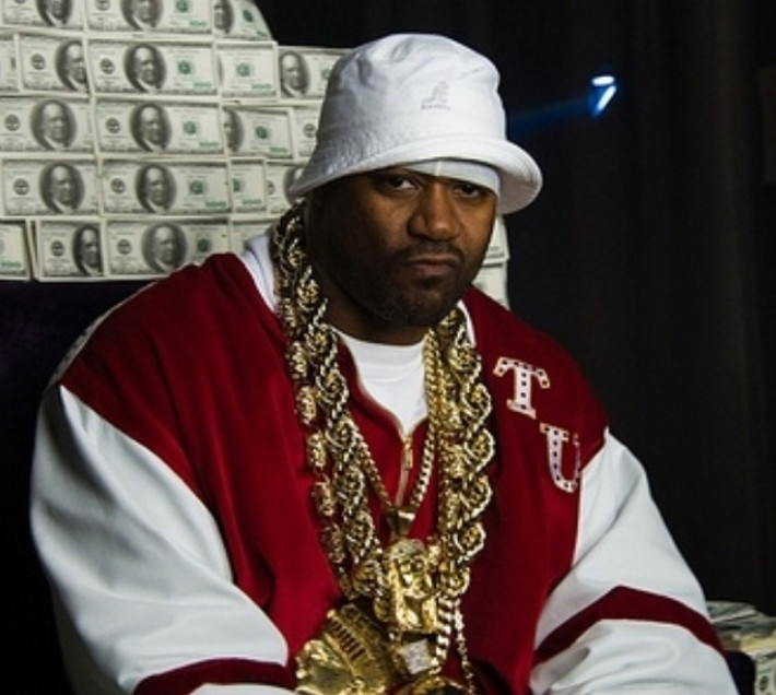 Ghostface Killah, wearing the following: \n\nA large baggy red and white zip up hoodie.\nA gray doo-rag.\nA white bucket hat over the doo-rag.\nAt least three phat gold chains, each rope thicker than the next, all with their own medallion. \n\nGhostface does not look happy to see you.