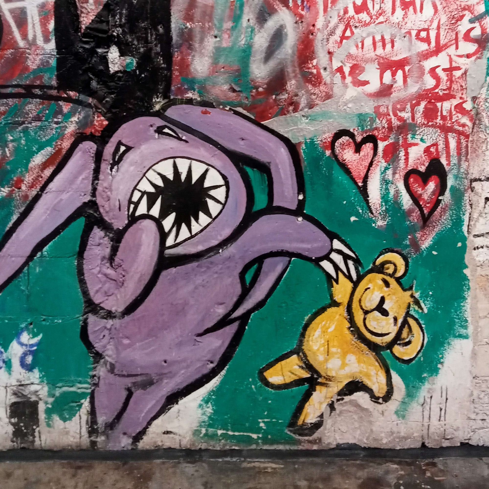 Graffiti of a scary, violet coloured comic figure holding a beige, smiling teddy bear