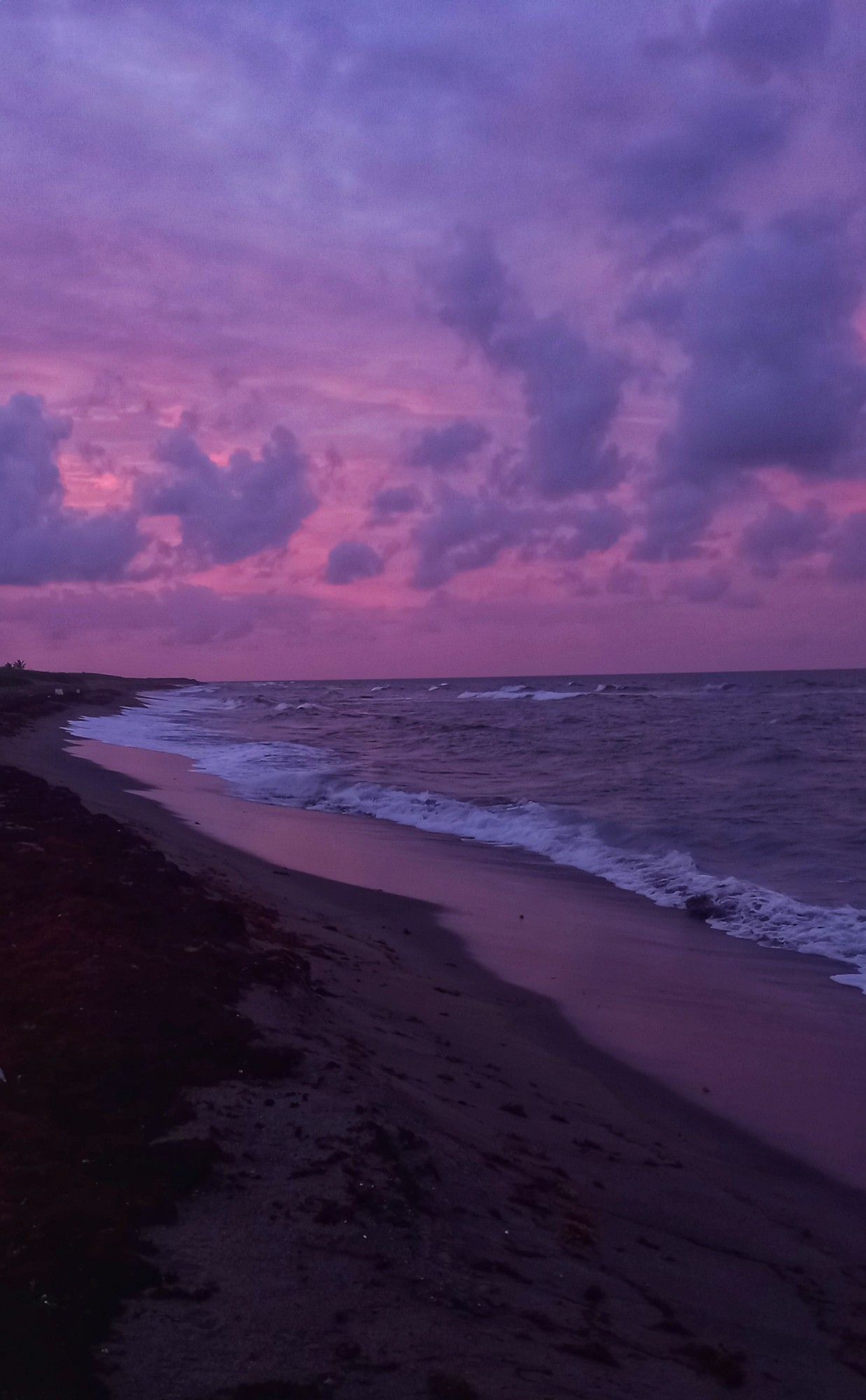 A mauve colored sky reflecting on a beach and sand