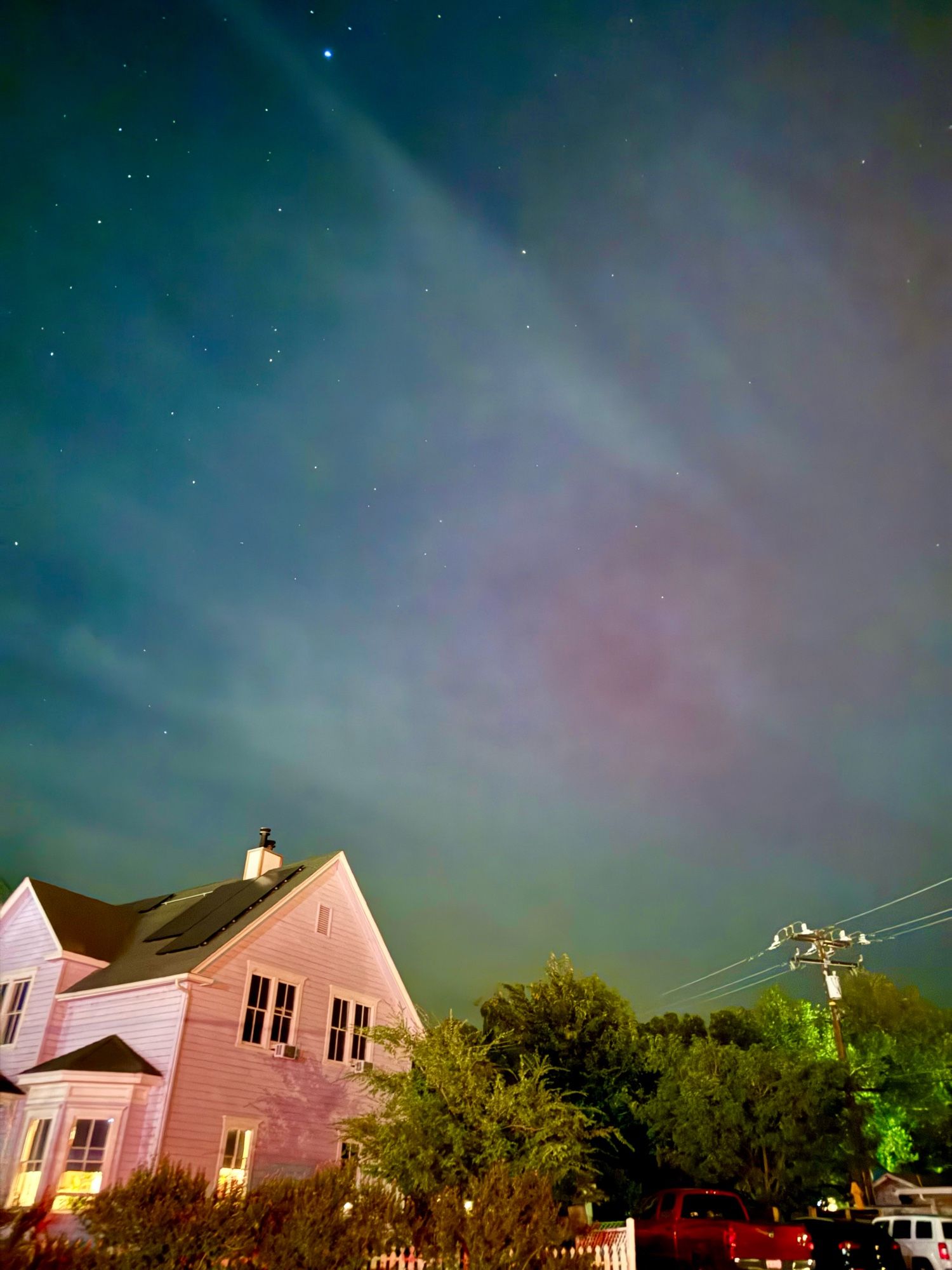 The night sky with stars over a pink farmhouse and then a faint splash of purple in the middle that is the aurora