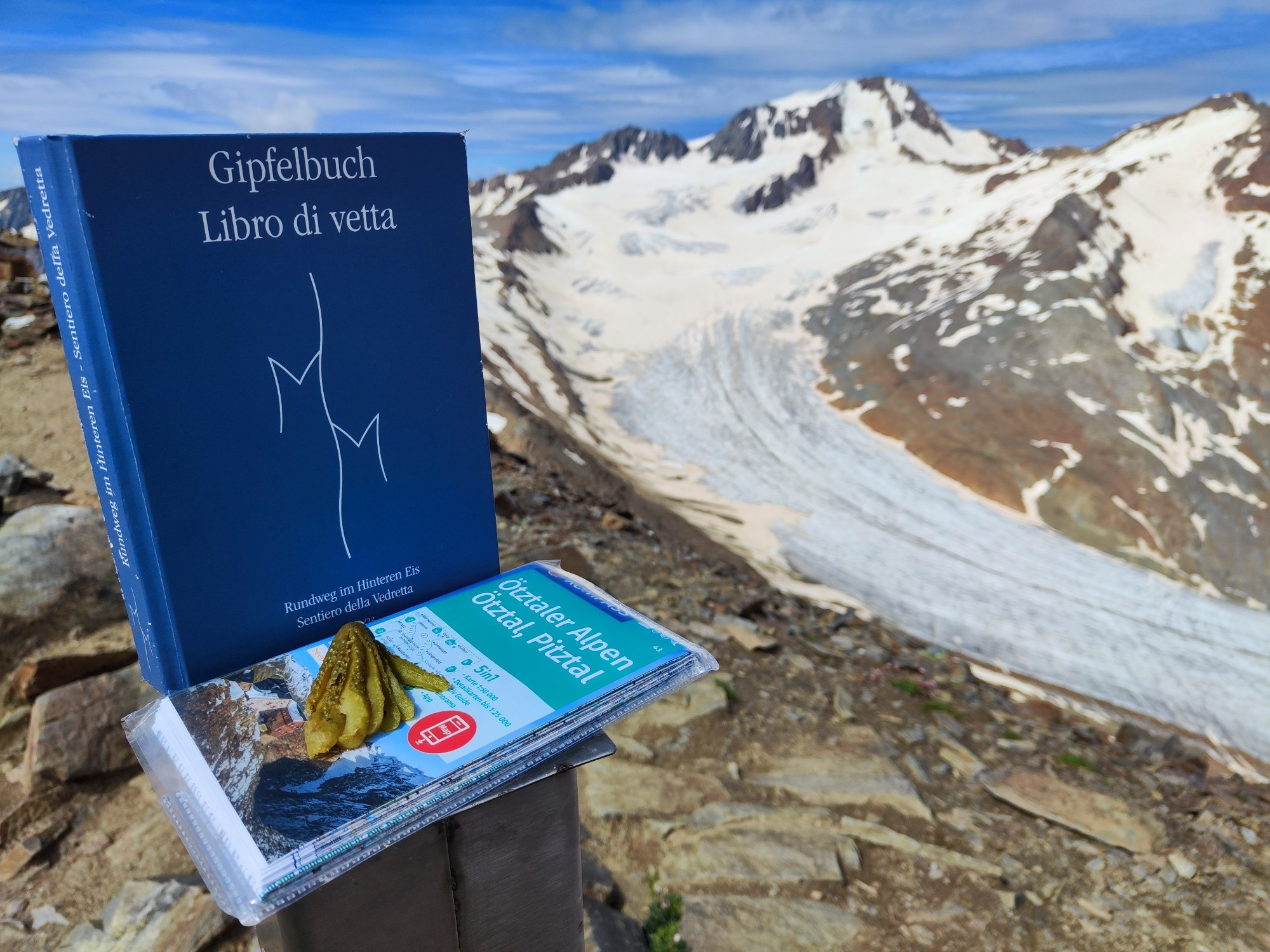 Gefächerte Gewürzgurke auf einer Landkarte, daneben steht das Gipfelbuch des Punta della Vedretta, im Hintergrund sind der Hintereisferner Gletscher und die Weißkugel