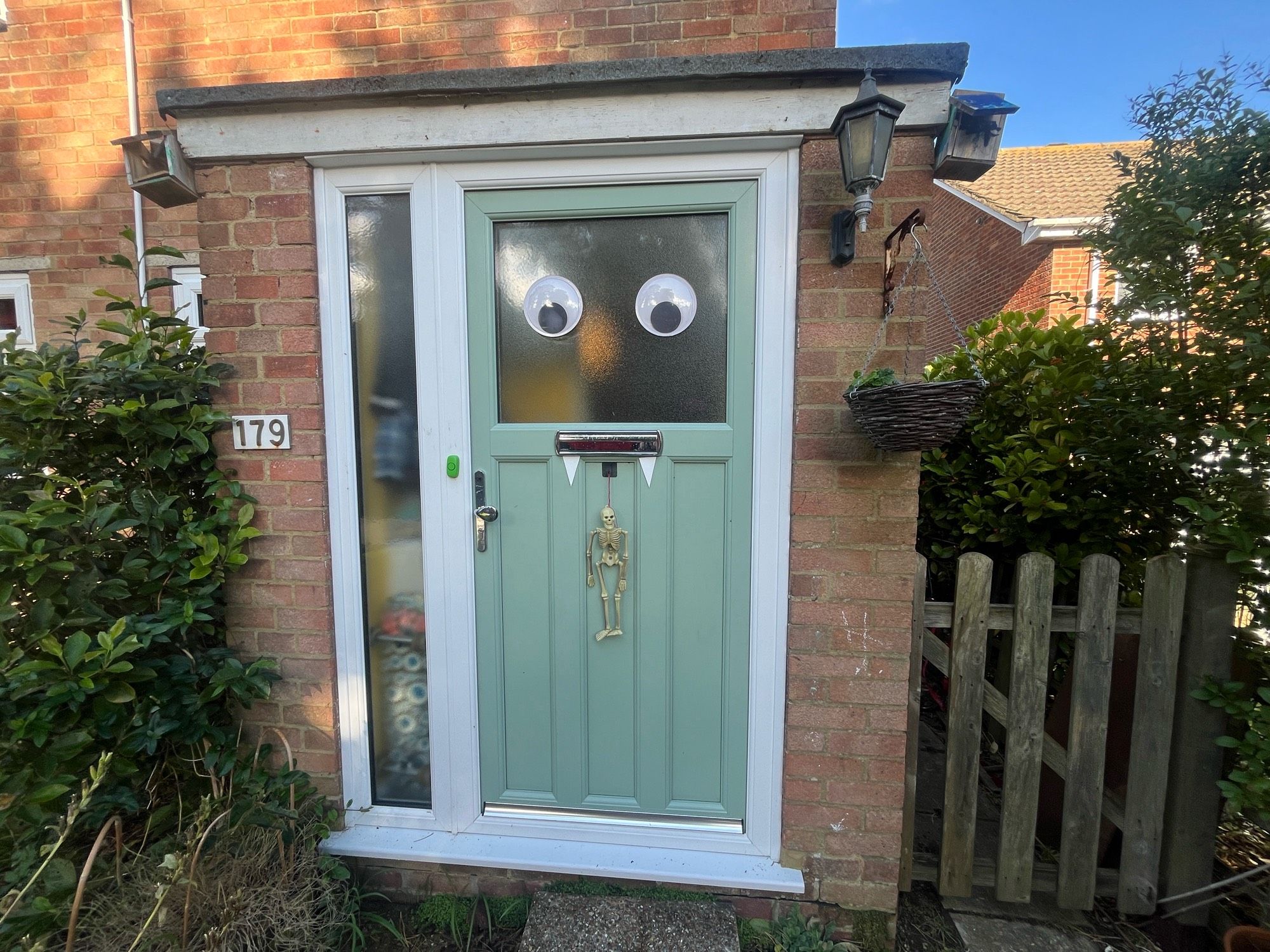 An external picture of a front door… the front door has two 7-inch googly eyes attached to it, and small ‘fangs’ poking out of the letterbox, which looks like the mouth to go with the eyes.

A small plastic skeleton decoration is also hanging on the door below the letterbox.