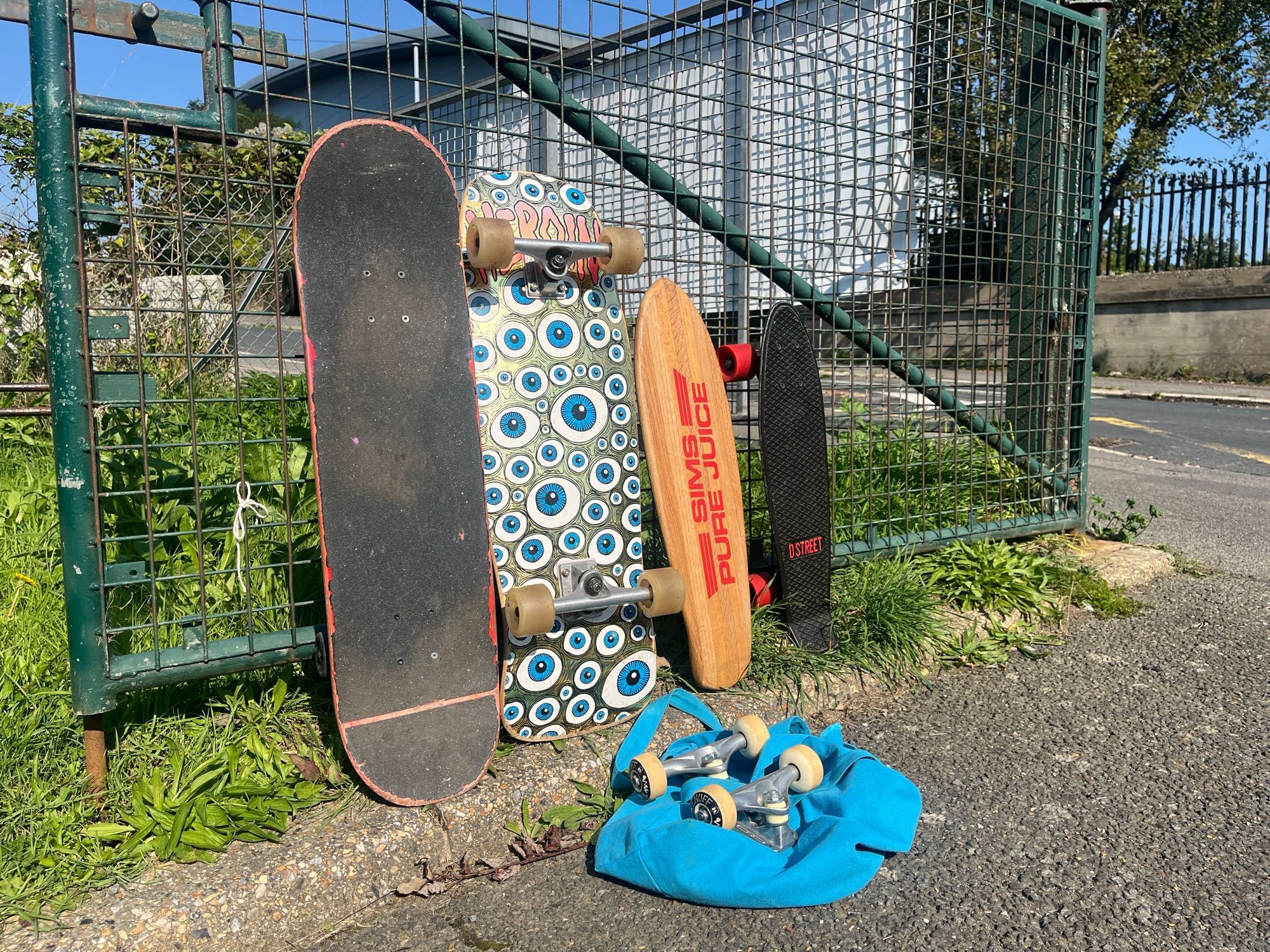 Four skateboards and some spare skateboard trucks and wheels lent against a fence.