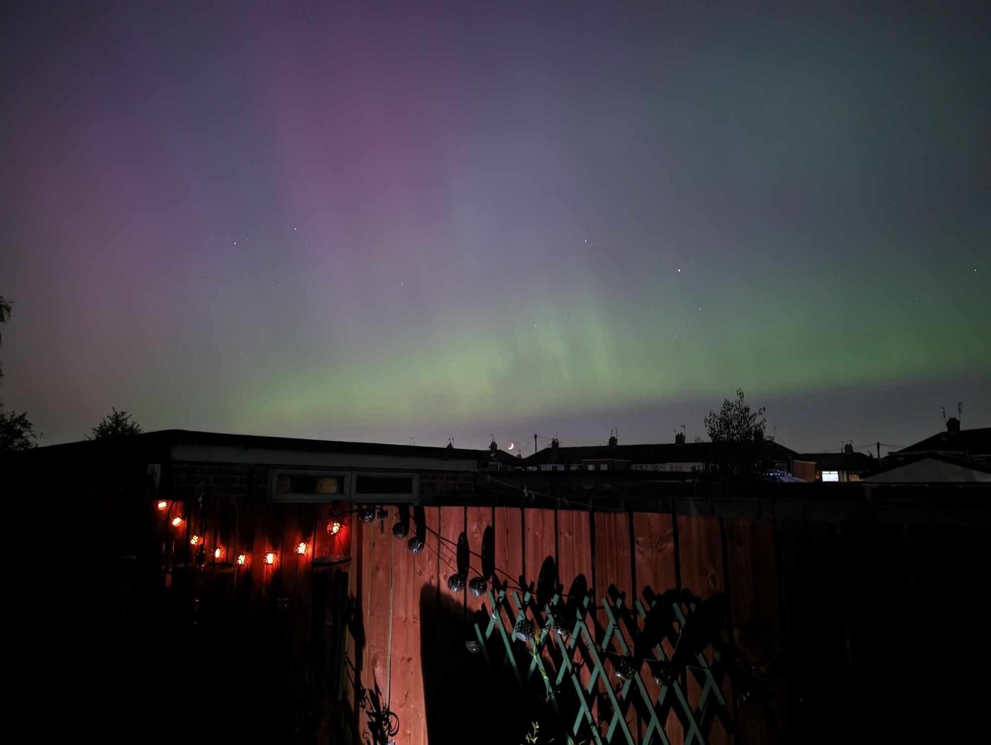 Green and purply red aurora above a setting crescent moon