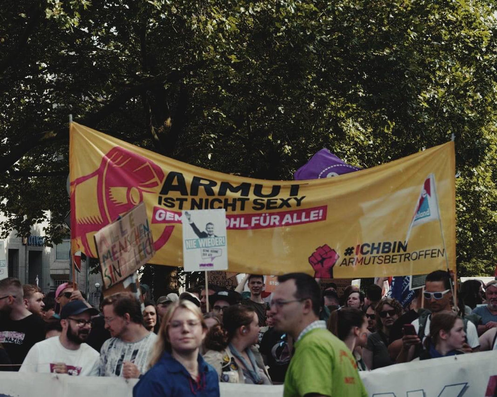 Foto: Mitten im Demozug ganz präsent an vorderster Front ist das gelbe Protest-Banner von #IchBinArmutsbetroffen gehisst.