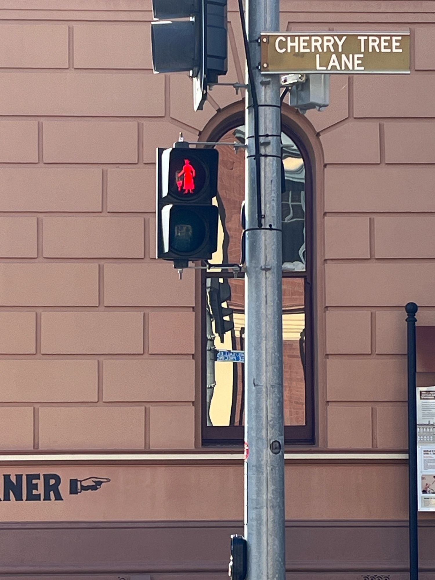 Pedestrian crossing signal on street corner in Maryborough, Queensland. The signal light is showing a customised red silhouette of Mary Poppins, holding a folded umbrella at her side to indicate she is not moving.