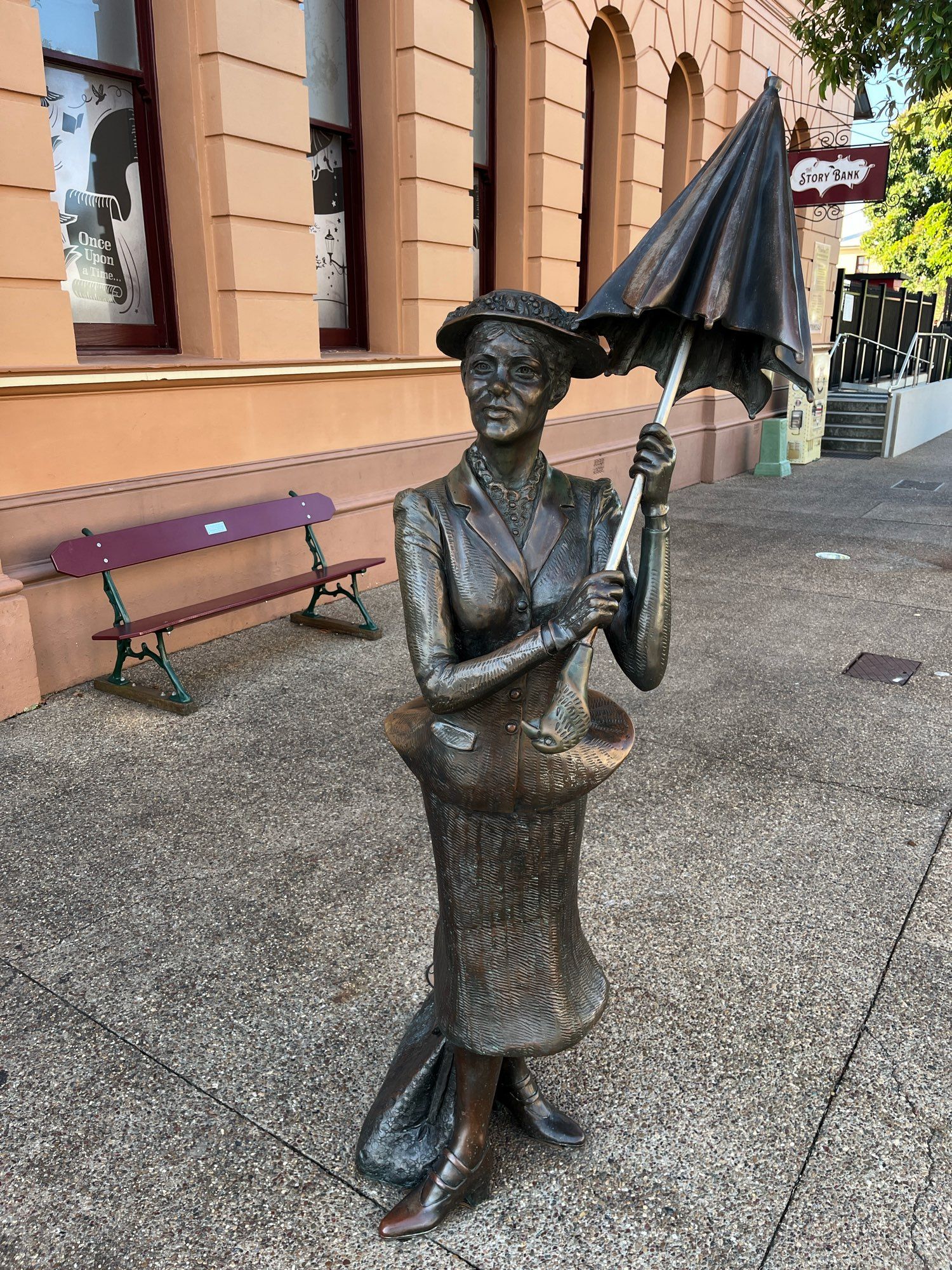 Bronze statue of Mary Poppins, umbrella aloft, on the footpath outside an old bank building in Maryborough, Queensland.