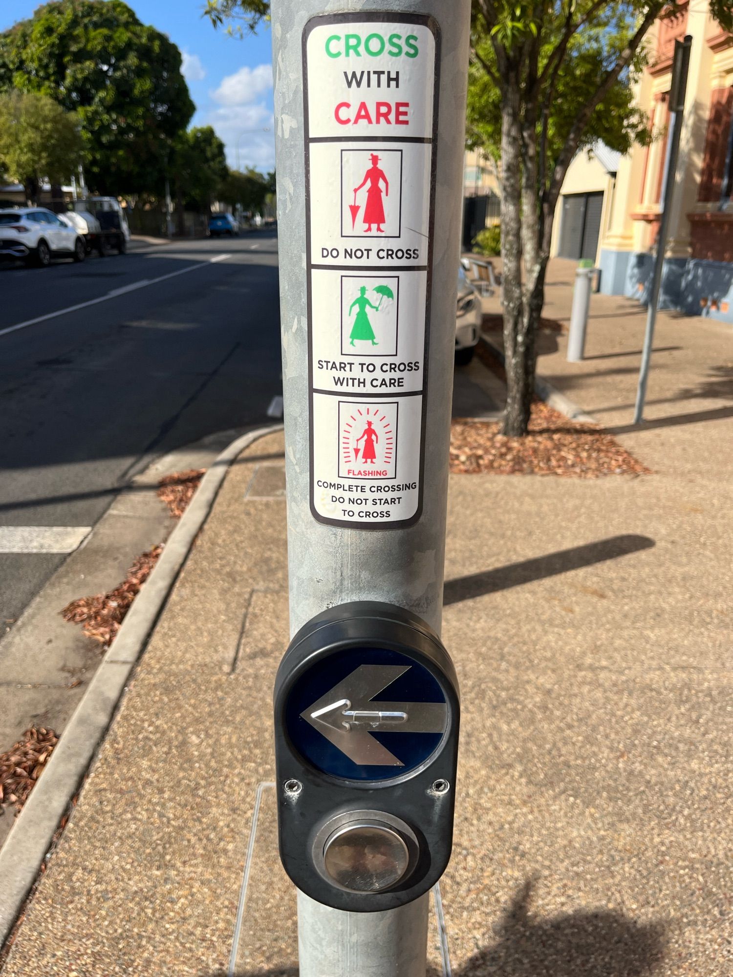 Pedestrian crossing button on pole with associated sticker indicating crossing rules with a silhouette of Mary Poppins, complete with umbrella.