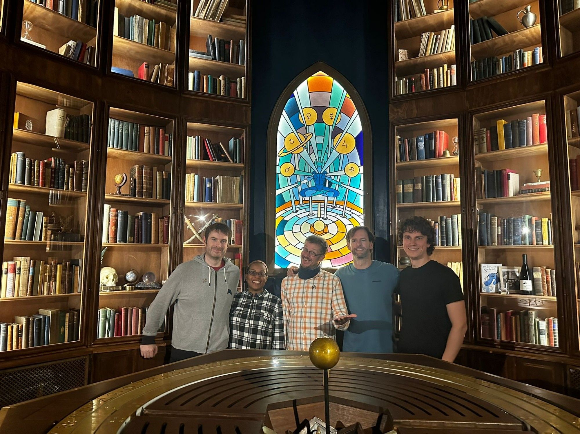 Team Photo in front of a huge library set with a stained glass window in the middle