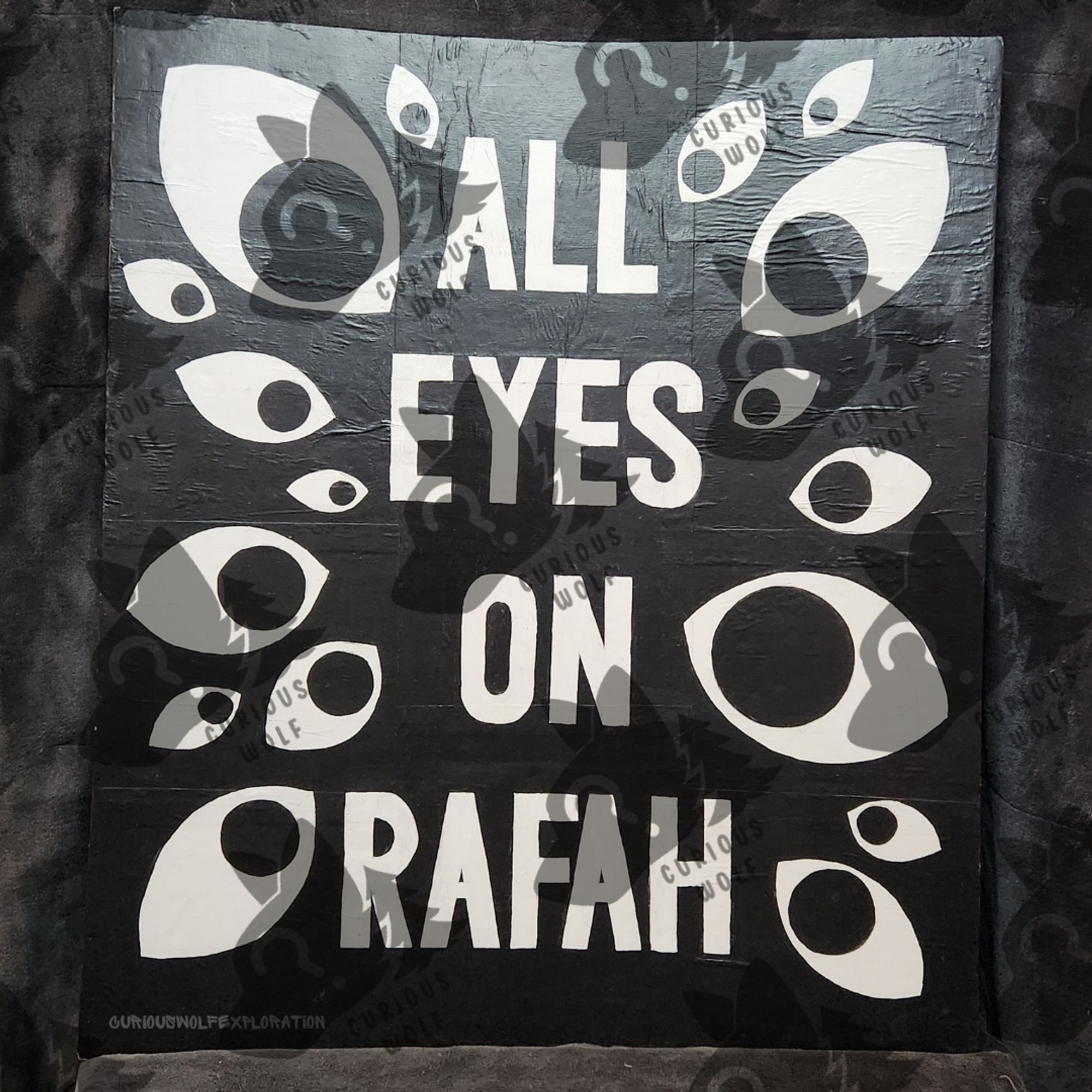 Sign Reading "All Eyes On Rafah" with 17 eyeballs all looking towards the words, on a black background