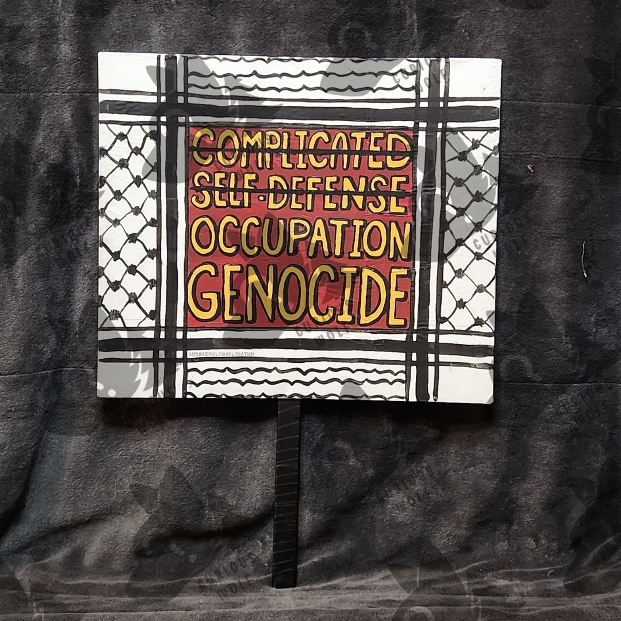 Keffiyeh design framing, Yellow words on a red background 

Words crossed out : Complicated, Self-Defense
Corrected words: Occupation, Genocide