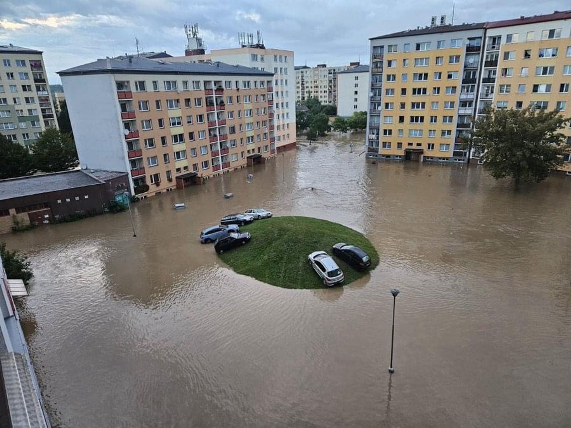 Several cars on an intercity island that is surrounded by flooded buildings