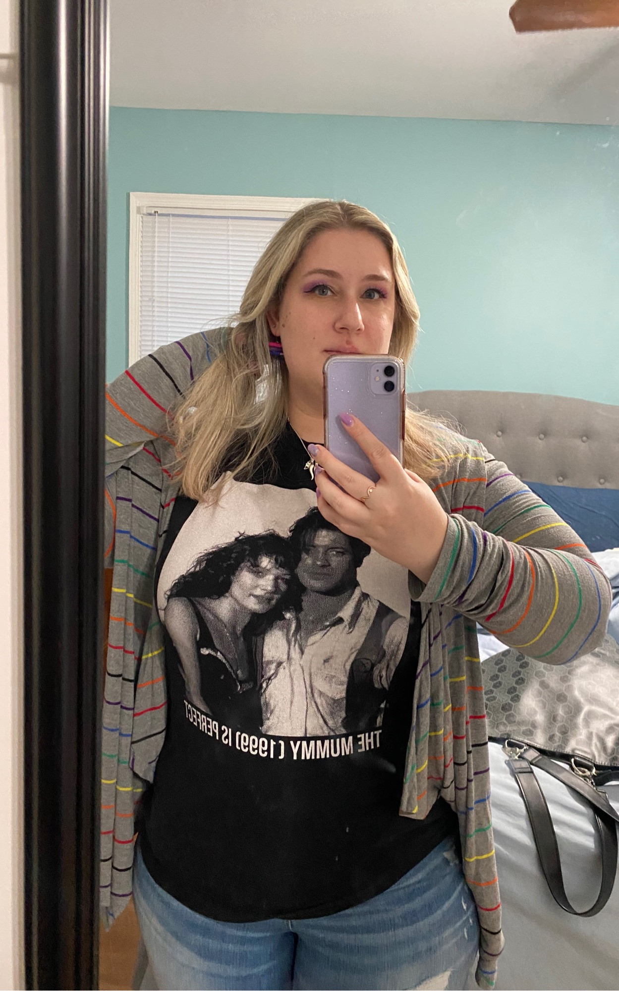 Mirror selfie of me in a The Mummy (1999) Was Perfect tshirt from SuperYaki, with a grey and rainbow cardigan, and book earrings in the bi flag colors.