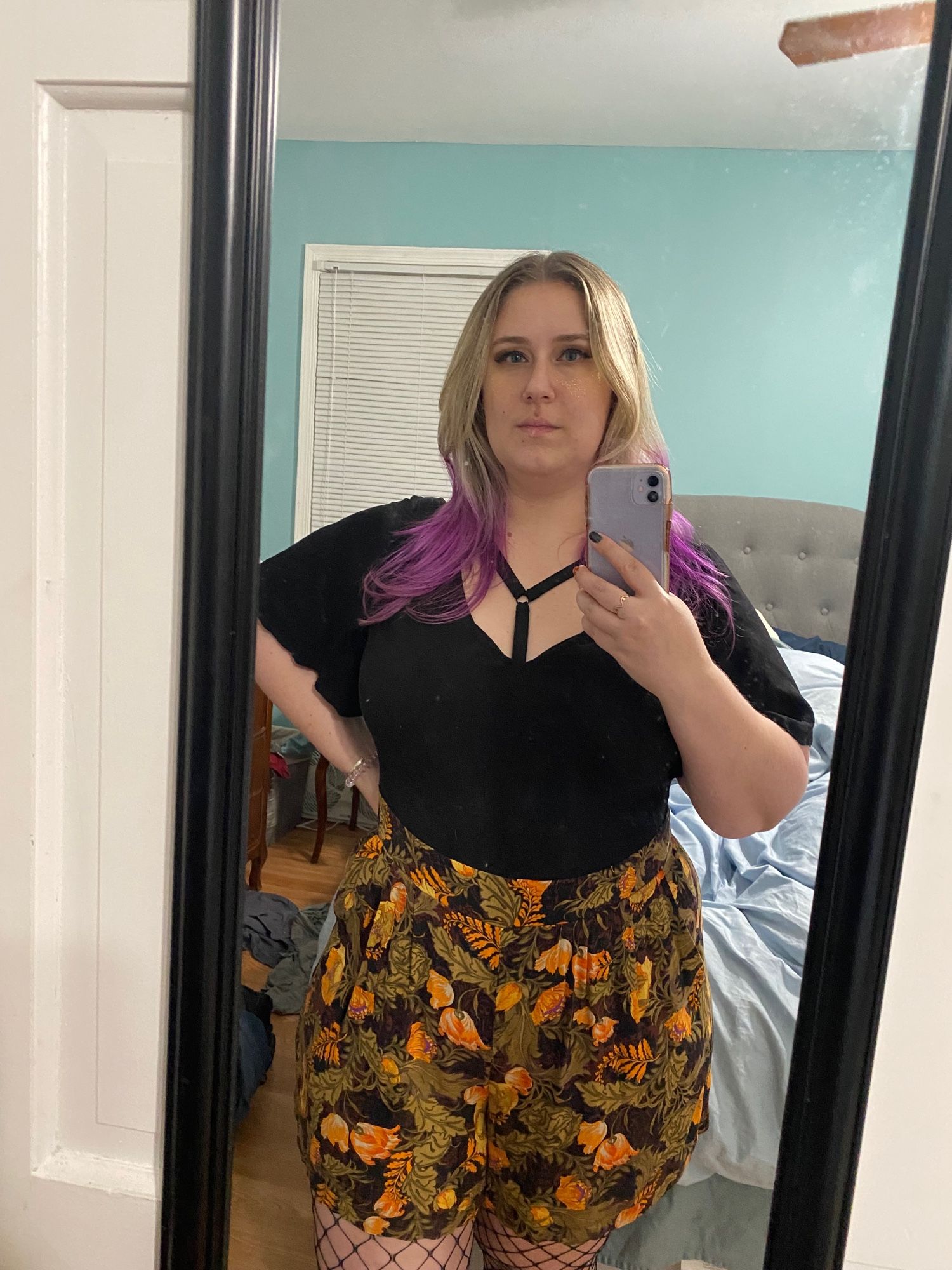 Mirror selfie of me in a black and orange detailed romper with fishnets underneath. The ends of my hair are ombré purple and I have a harness peeking out from under the romper. If you’ve seen me wear this outfit before, no you haven’t.