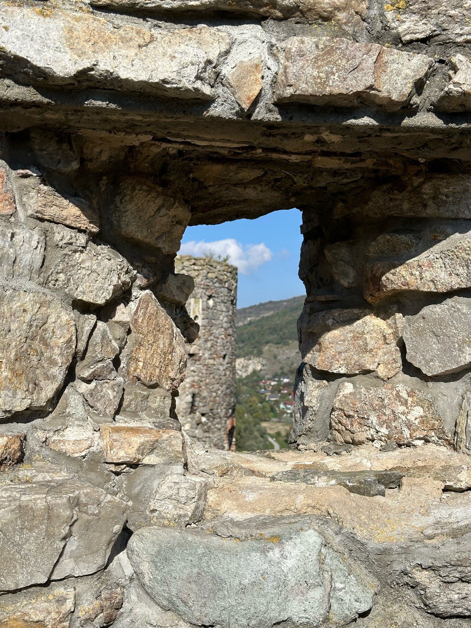 Looking at a castle tower through a window hole from the ruins