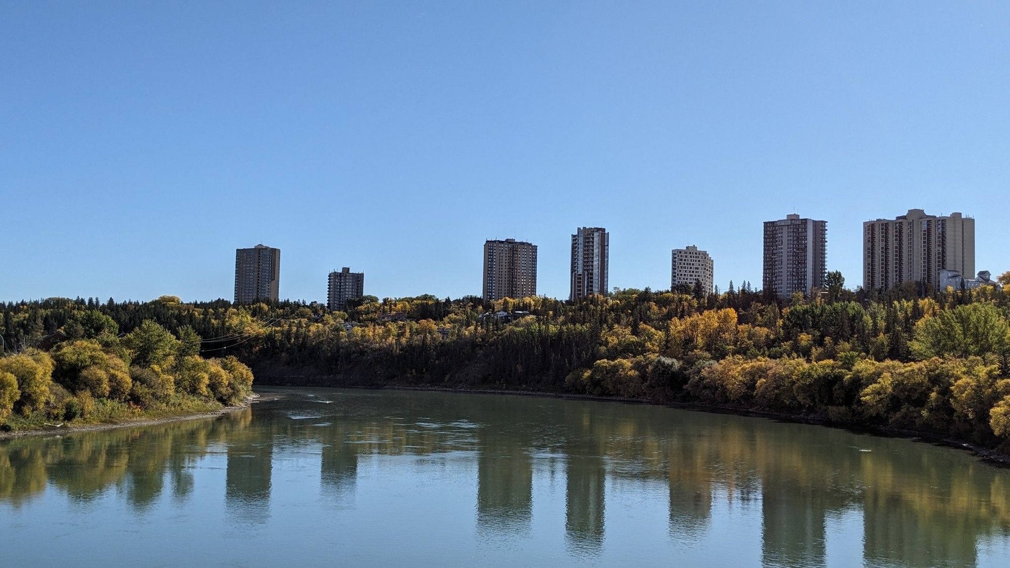 A river valley scene with fall colors and the buildings in the distance are reflected perfectly in the river