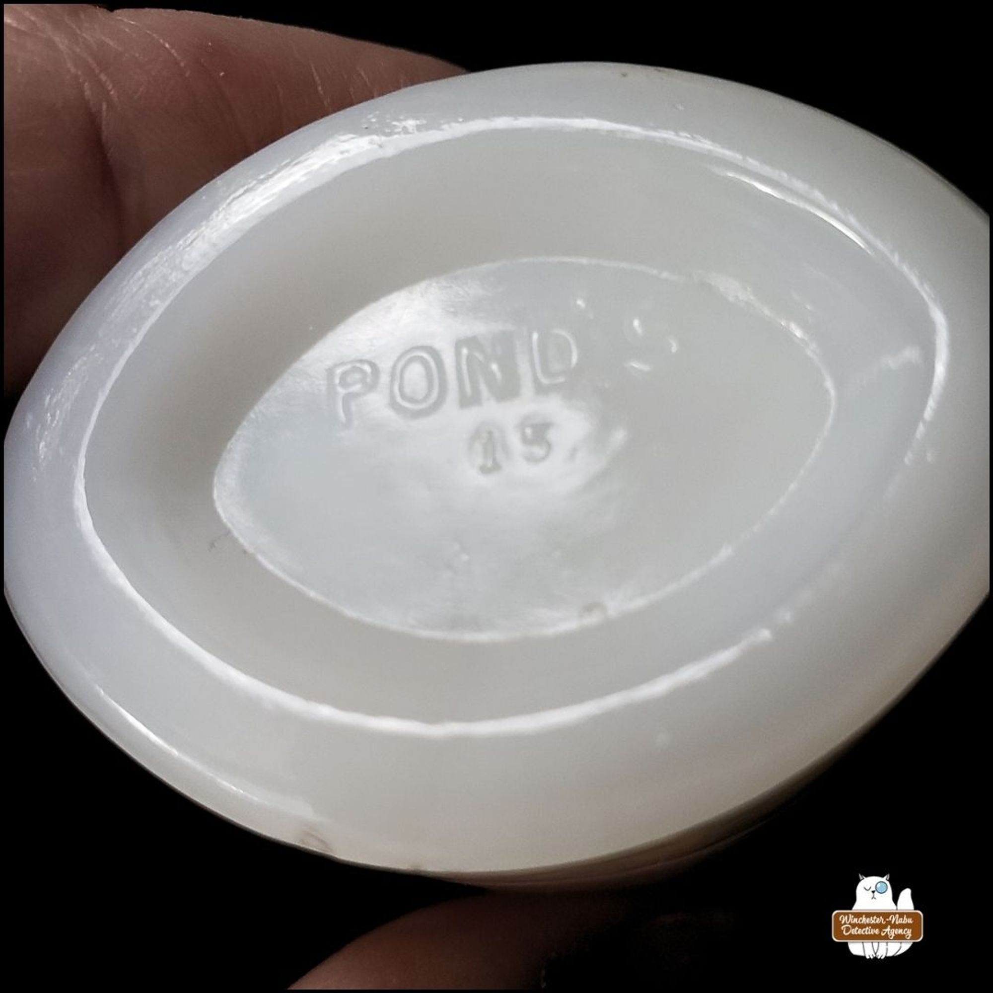 the bottom of the Pond's milk glass jar photographed at an angle to best show the embossing; shows the word Pond's and two characters underneath