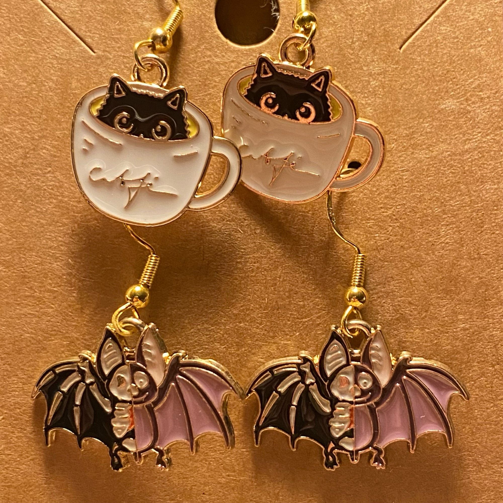 two pairs of dangly earrings first of black cat in coffee cups and second is bats. earrings by my squish studio