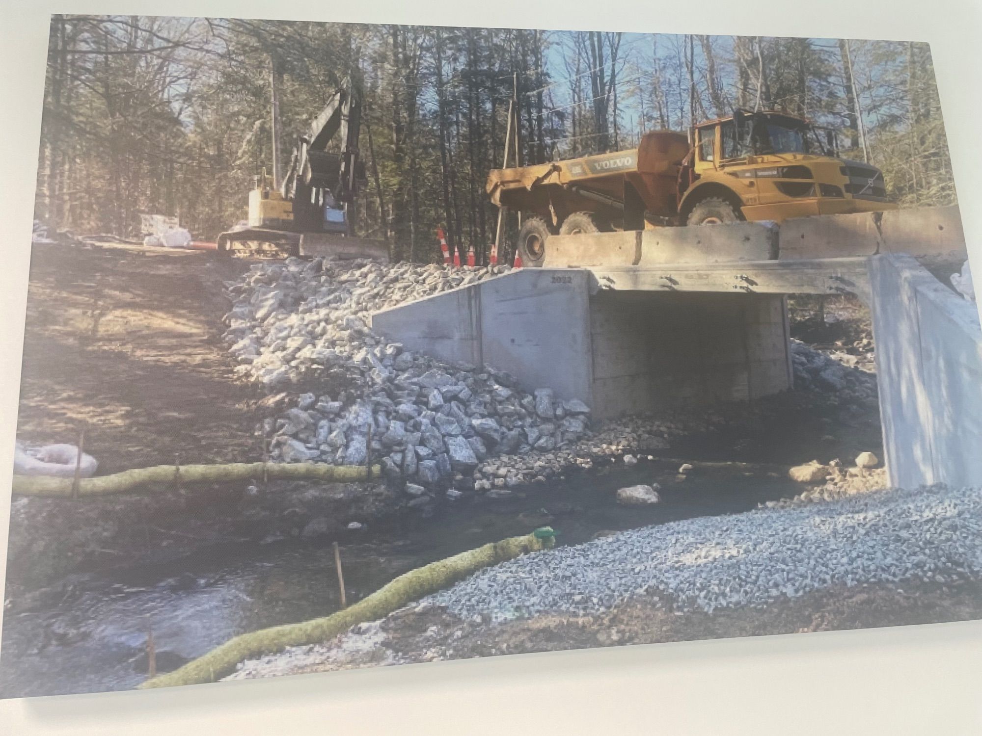 A large excavator and dump truck parked on top of a newly constructed culvert, channeling a stream with improved flow controlled primarily by a restored culvert slope, surface roughness, and tailwater elevation.