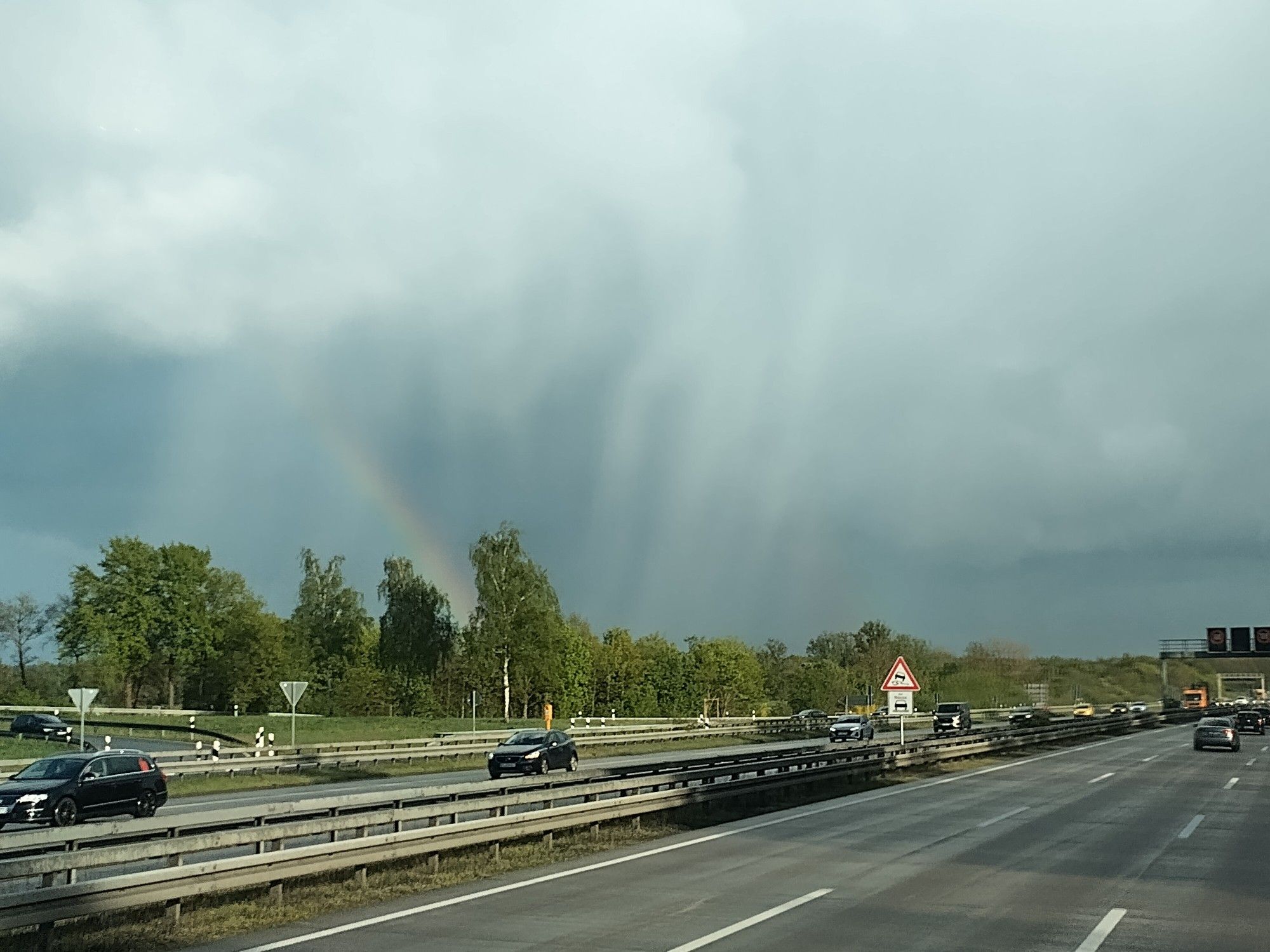 Regenwolken und ein bißchen Regenbogen über einer sonnenbeschienenen Autobahn.