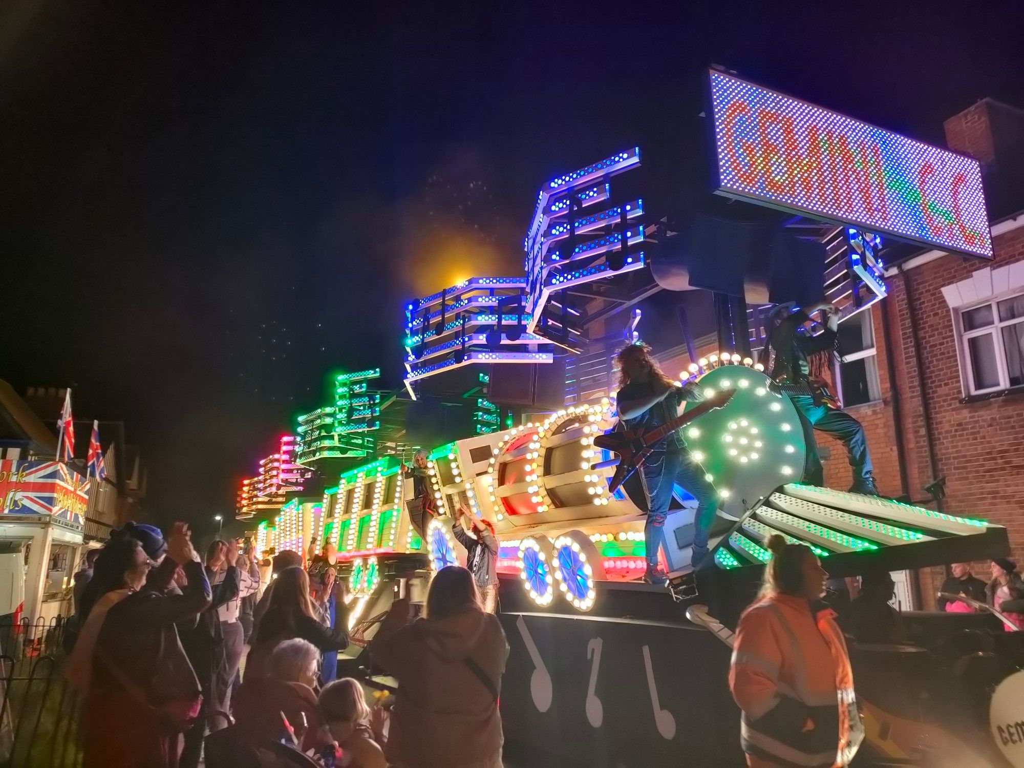 An illuminated carnival float made to look like a train with a rock music element.