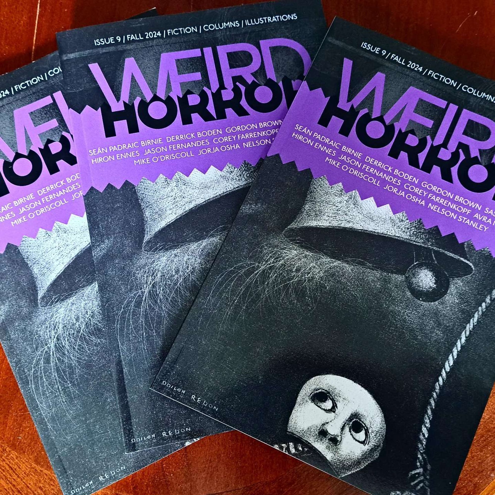 Copies of Weird Horror 9 on a coffee table. Cover art has a purple banner with black and white art by Odilon redon showing a skeleton ringing a large bell with a pull rope.