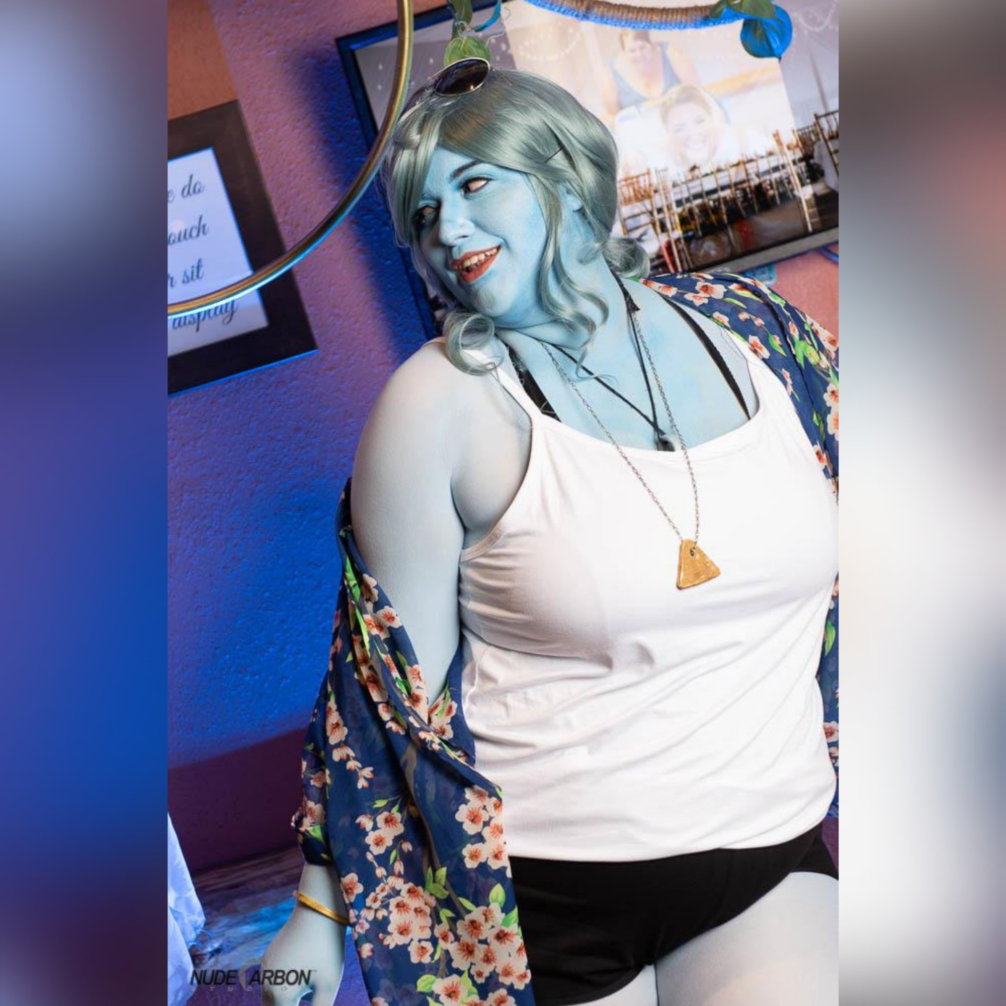 A cosplay! The woman in the picture is meant to be a ghost! She is depicted with light blue skin, light blue hair, and wears black booty shorts, a white tank top, and a floral over shirt. She has sunglasses on her head and a few pieces of jewelry. She looks like she's having a great time!