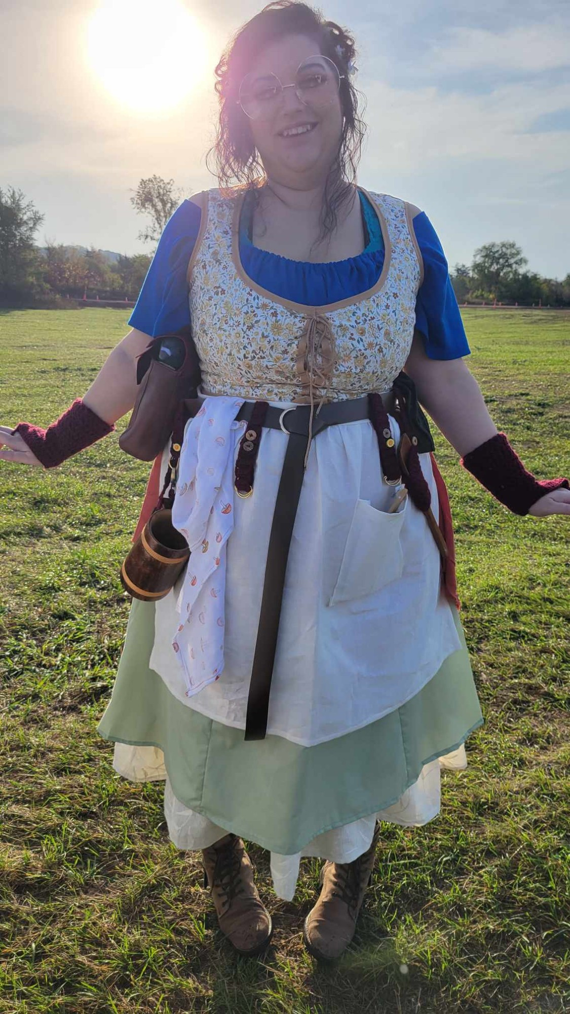 The concept art realized!  The femme human is wearing her hair up in messy buns, LARGE round glasses and elf ears.  She has on several layers of skirts (ranging from cream, to light green, to orange.  The stays are a floral print over top a blue shirt.  She has an apron and crocheted gloves.  and a pigeon peeking out of her bag (his name is Henry Potatocrisp)