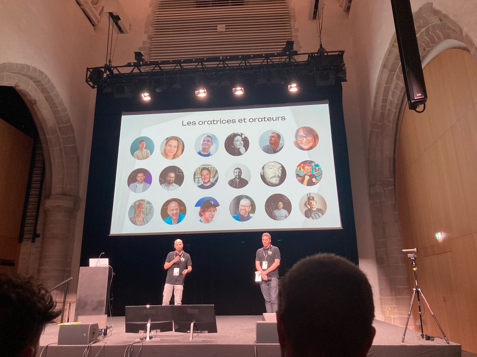 Deux organisateurs du WordCamp Bretagne sur scène, pour le discours d’ouverture. Derrière eux sur l’écran, la slide avec le portrait des oratrices et orateurs de la journée.