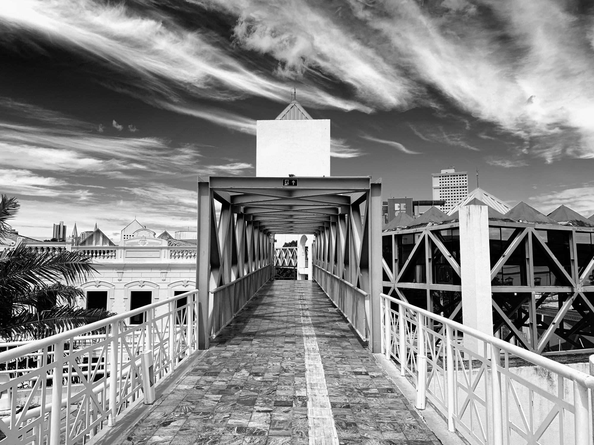 A square-shaped covered bridge, buildings in the background, sky with striking clouds.